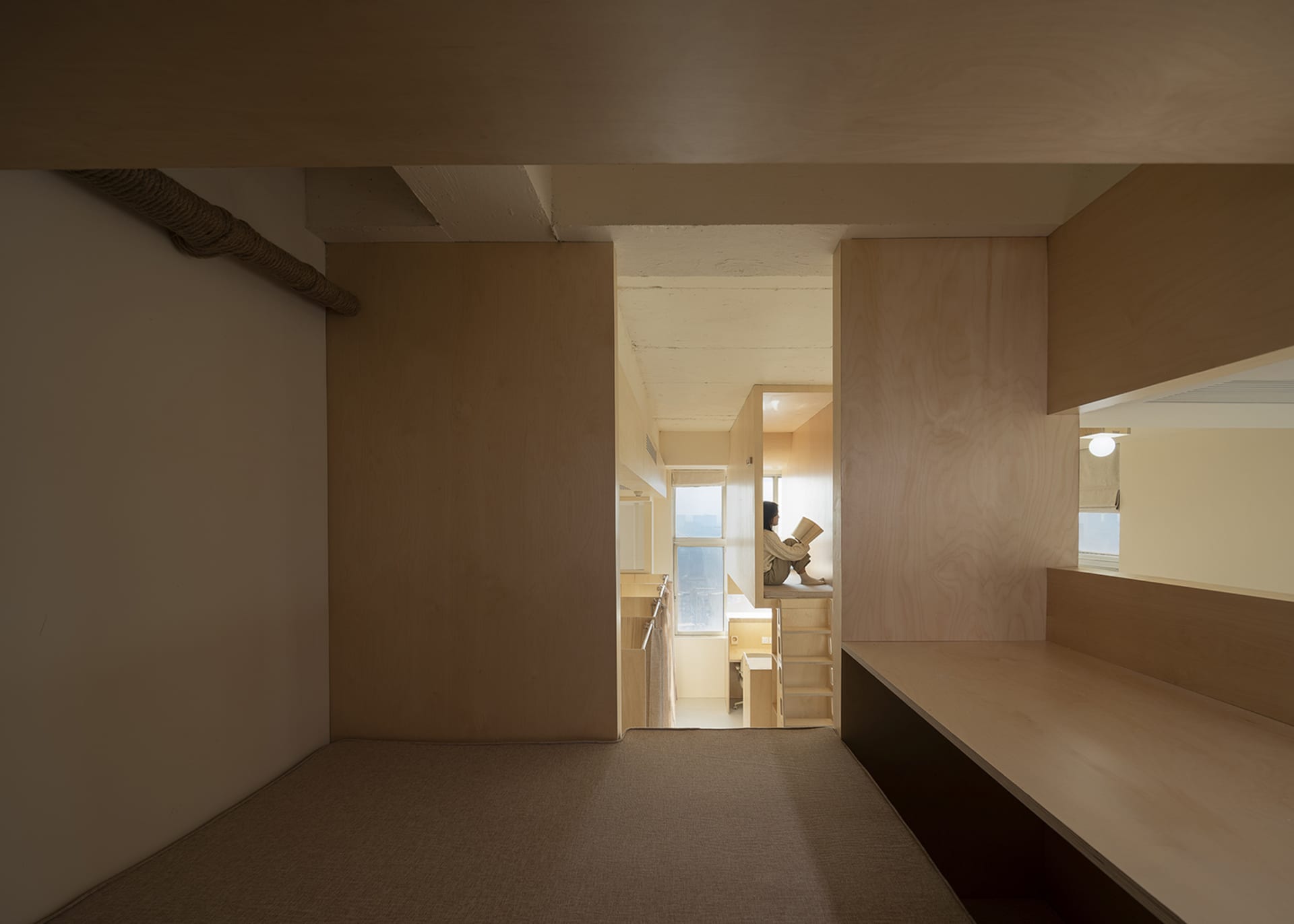 A modern minimalist living room featuring a wooden floor and walls, with a person sitting on a platform reading a book.