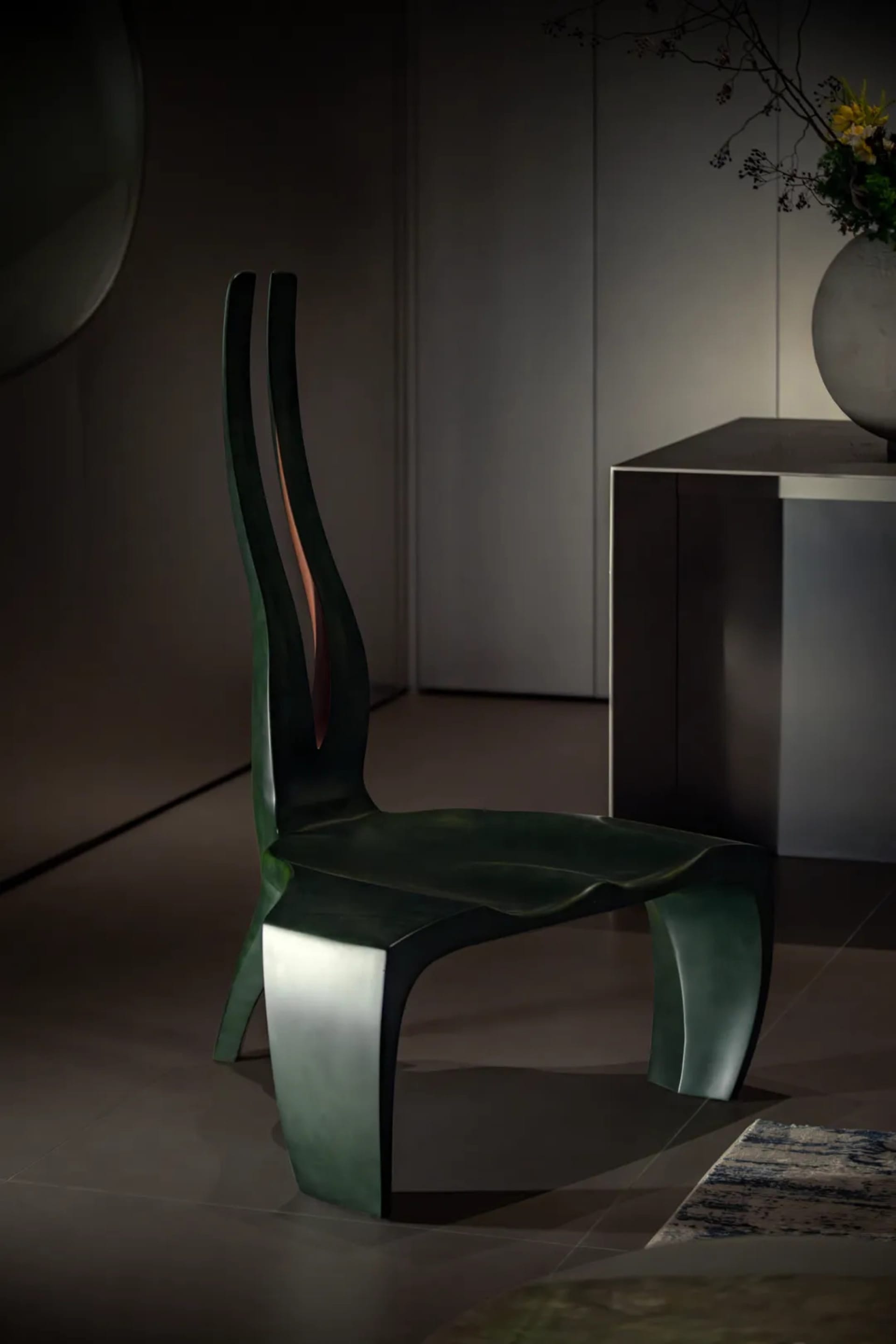 A sleek, modern metal stool with a grey finish, featuring curved lines and a unique shape.