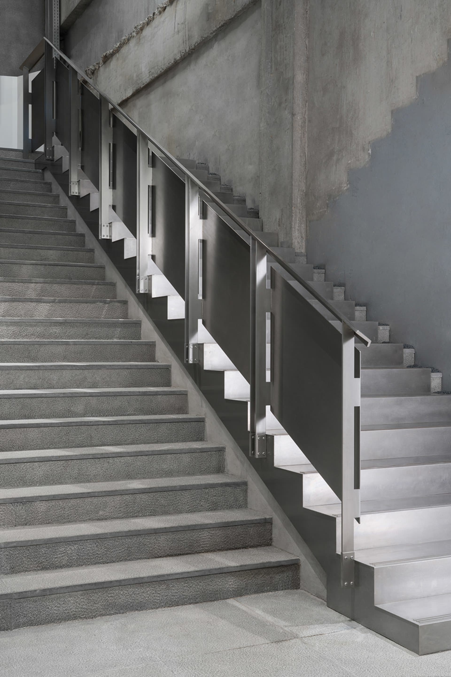 Staircase with industrial design, featuring metal railings and concrete steps on a concrete floor.
