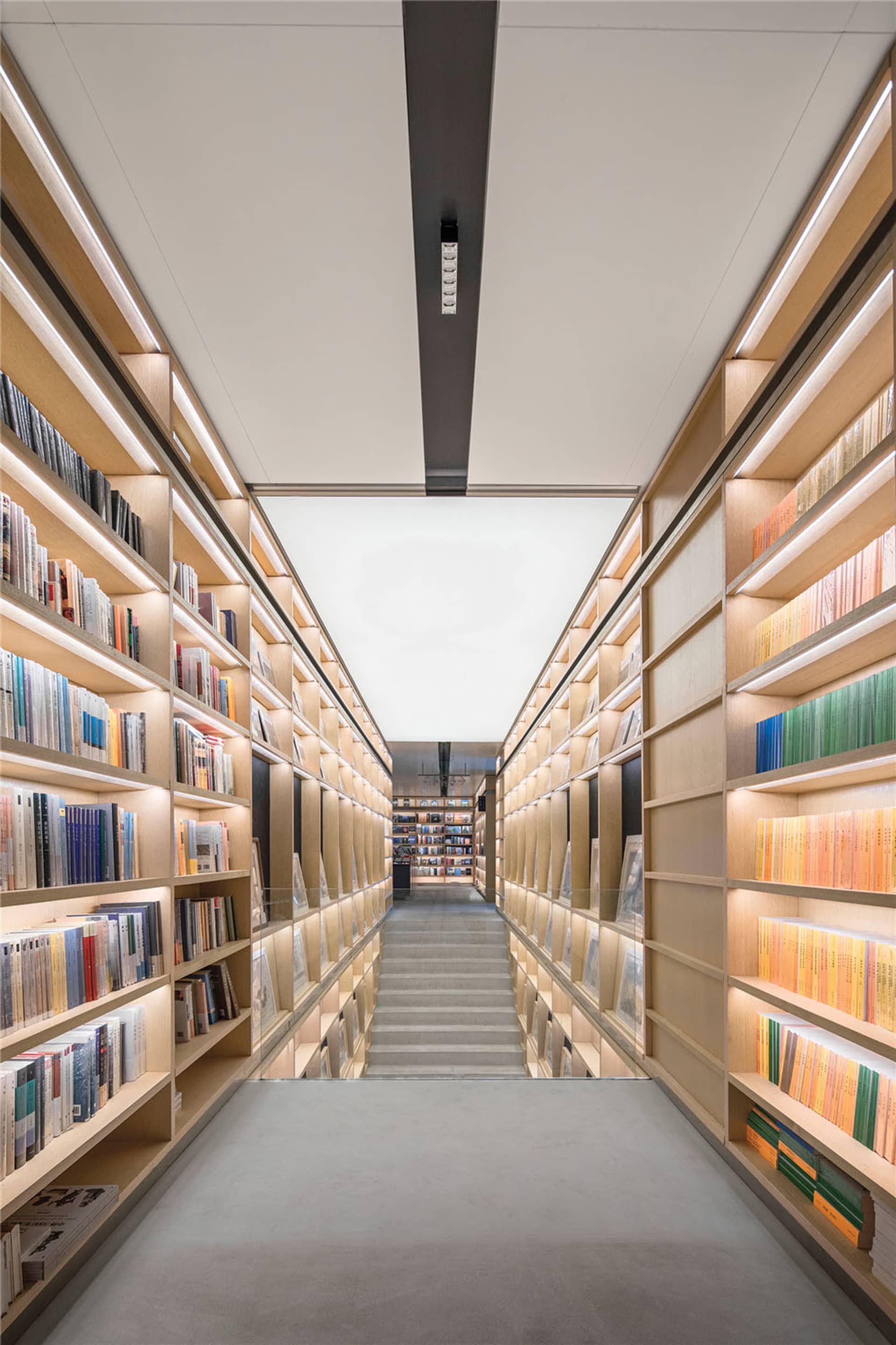 A modern, spacious library with tall bookshelves filled with books, illuminated by soft lighting from within the shelves.