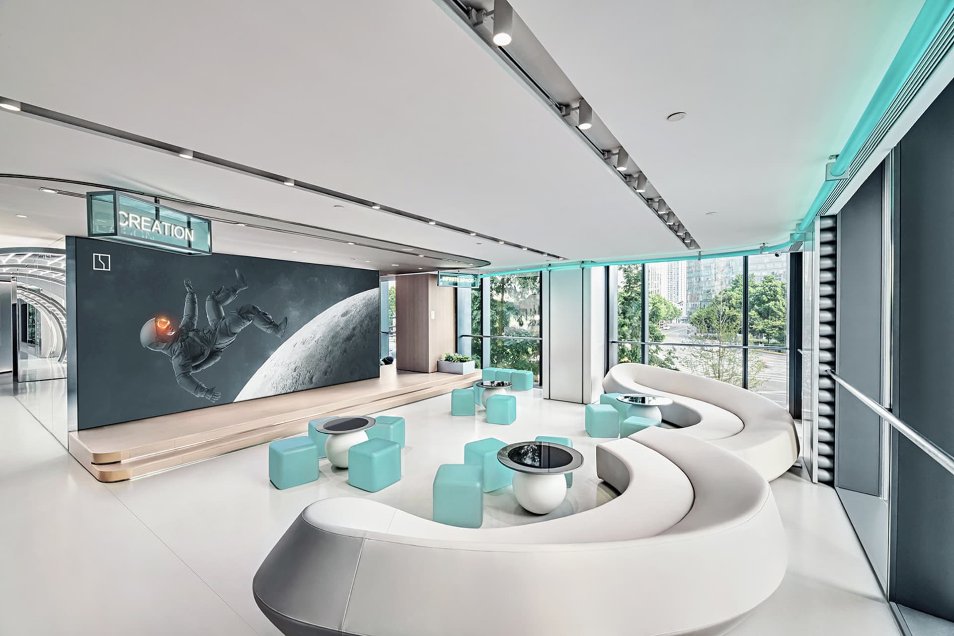 A modern office lounge featuring white and turquoise seating with concrete flooring and concrete seating areas, illuminated b