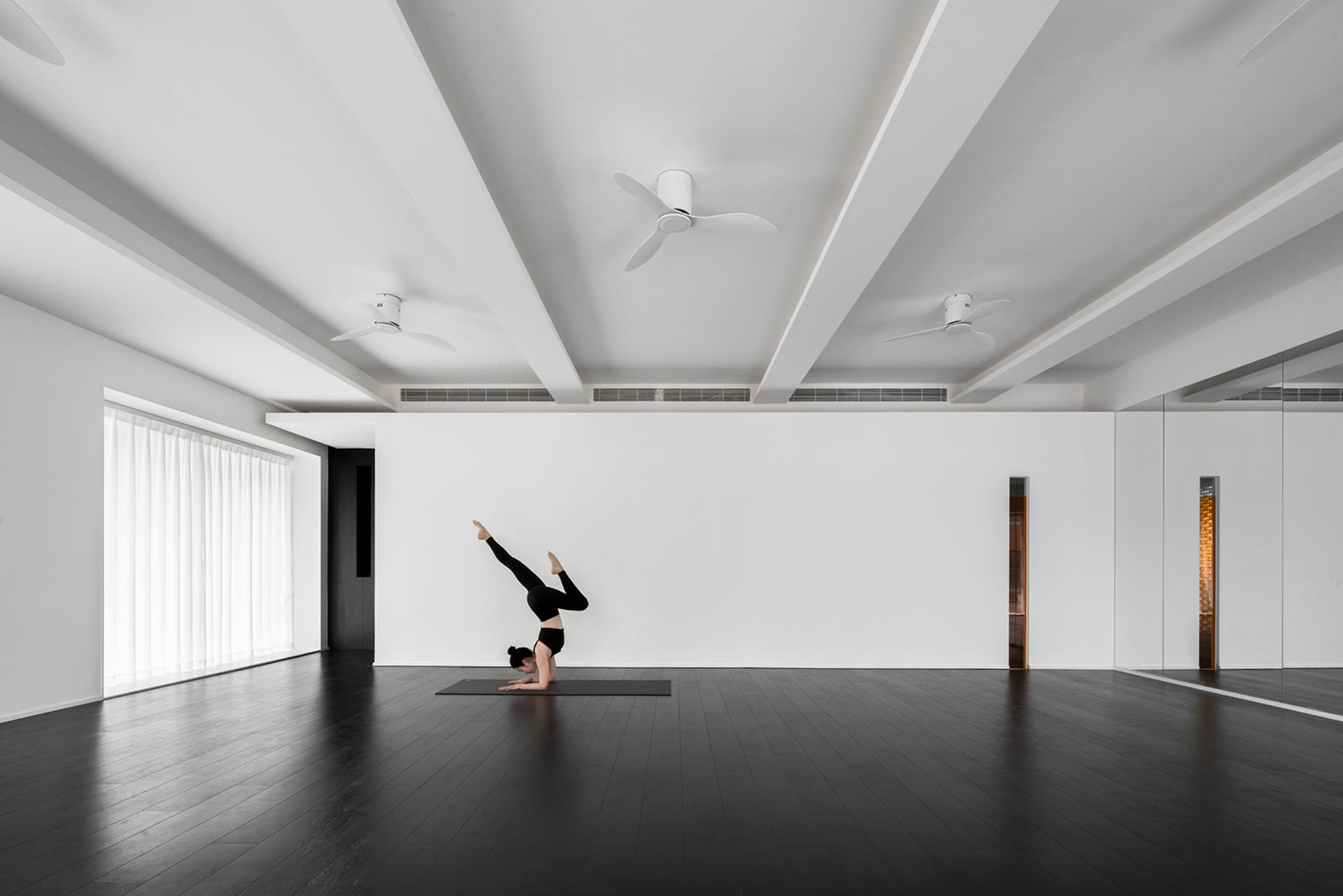 A woman performing a yoga pose in a minimalist studio with white walls and black floor.