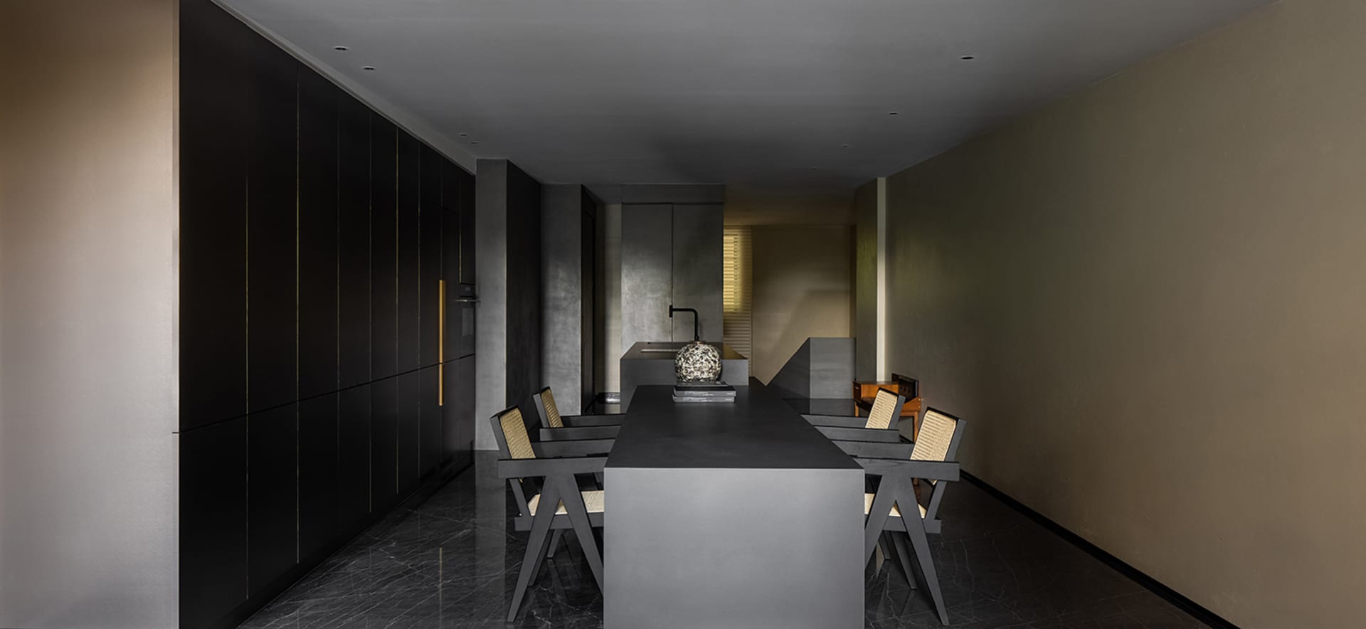 Modern minimalist kitchen with concrete countertops and floor, featuring sleek black cabinets and a central dining table with