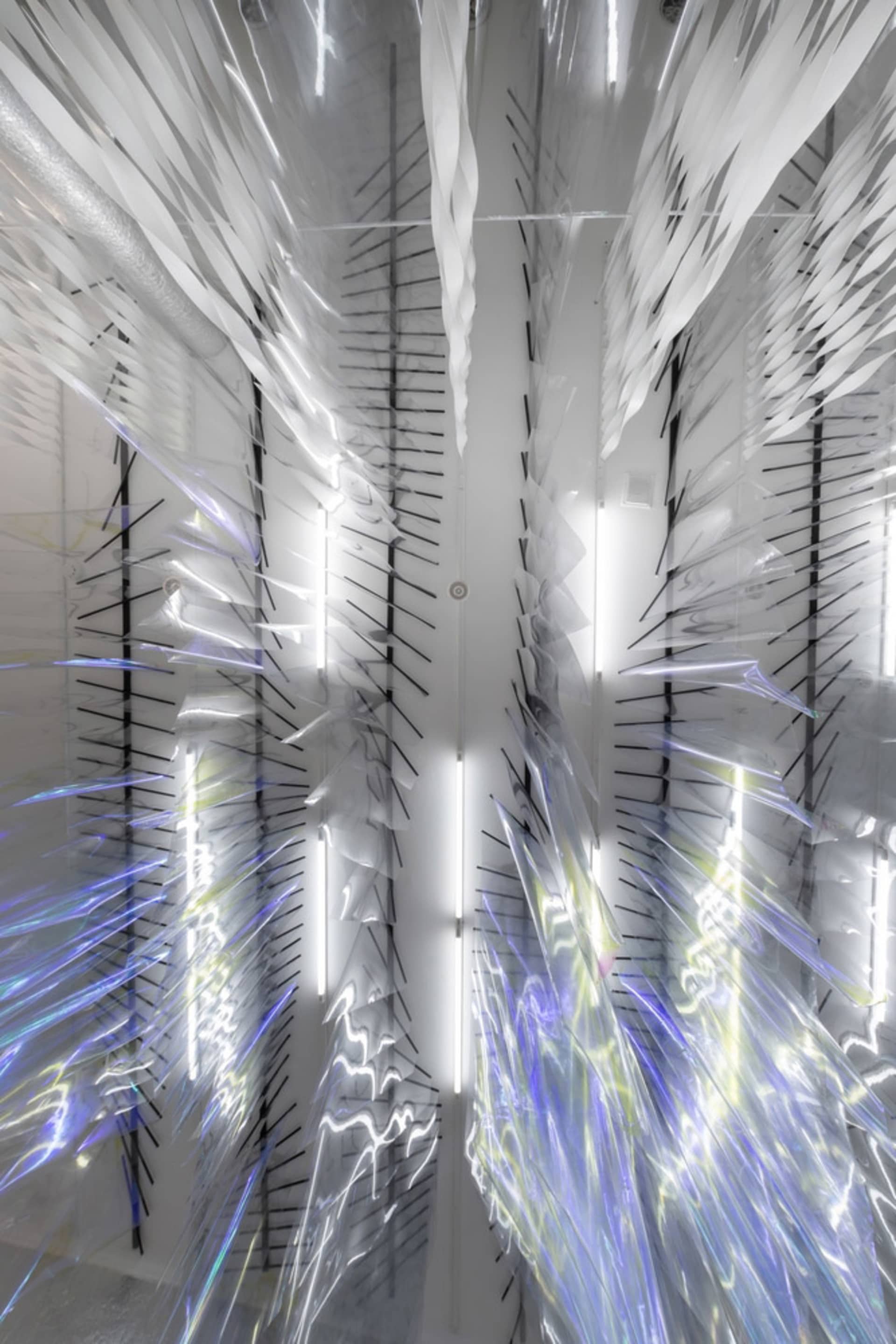 An abstract art installation featuring translucent, iridescent fabric panels suspended from the ceiling.