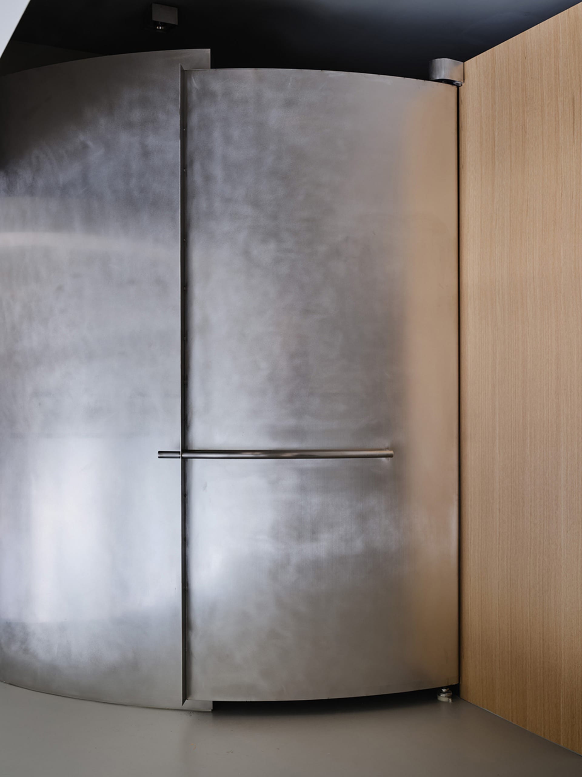 A modern metal door with a sleek, curved design, featuring a horizontal handle.