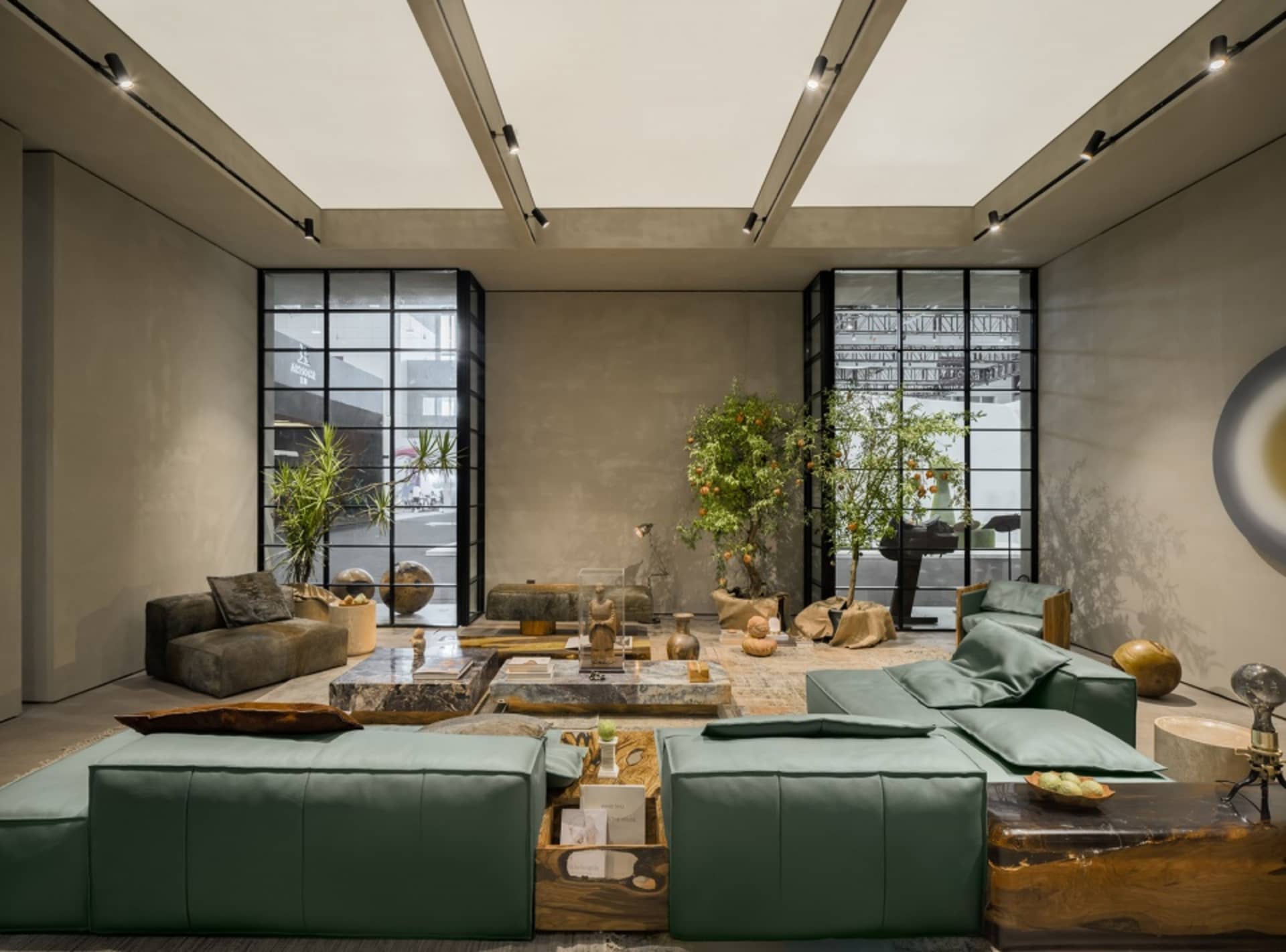 A modern, minimalist living room with concrete walls, furniture, and lighting, featuring green sofas and decorative plants.