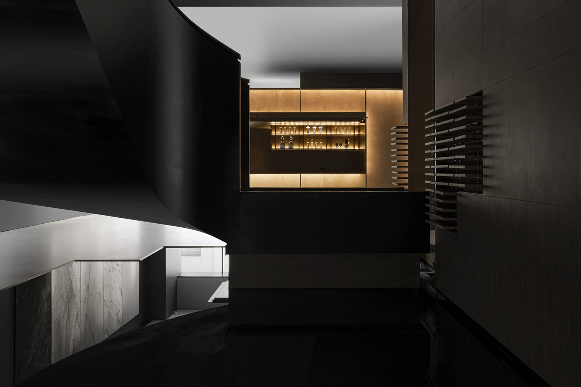 A modern bar area featuring wooden panels with dim lighting and bottles displayed on shelves.