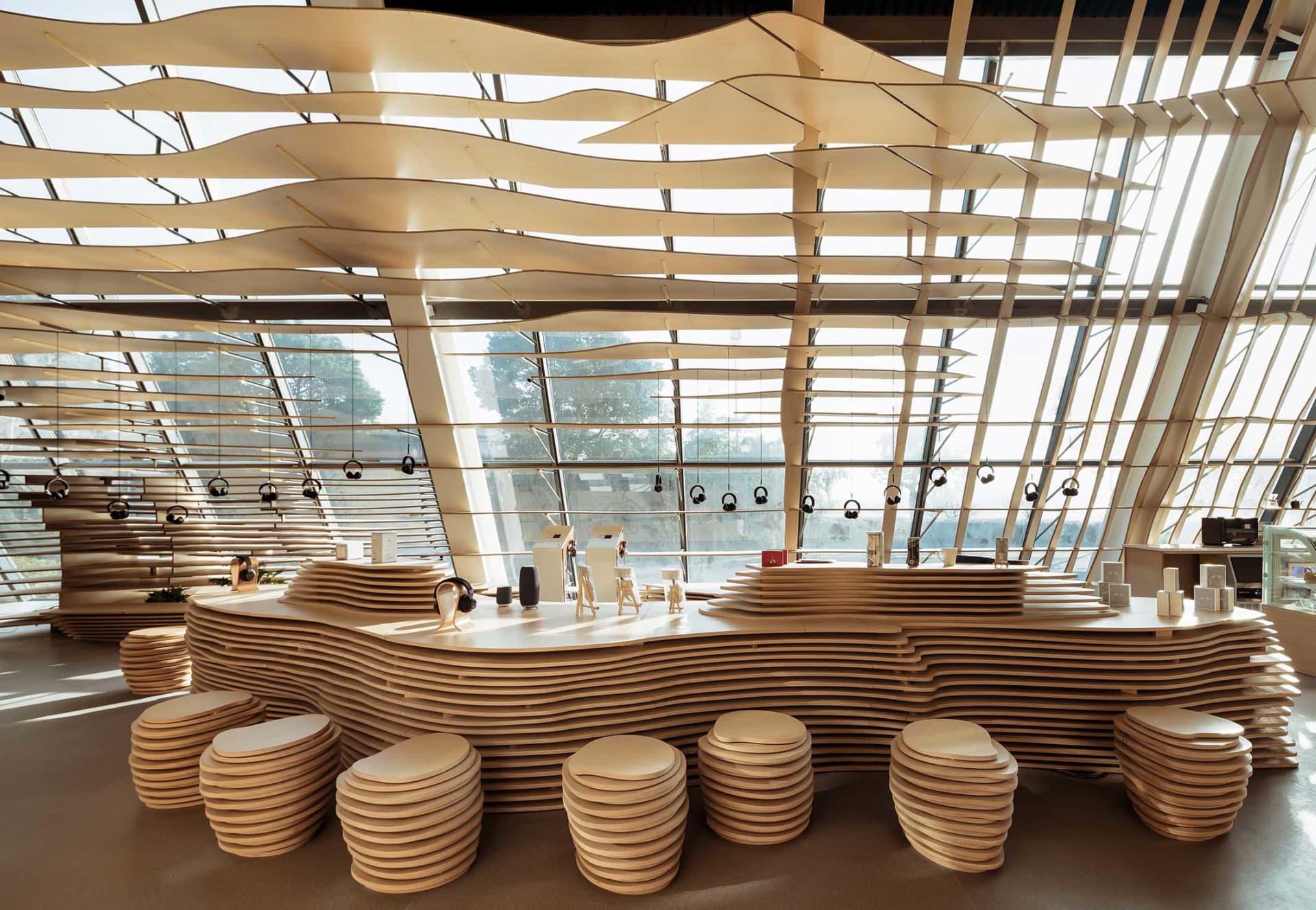 A modern coffee shop interior featuring a wooden wave-shaped counter and stools.
