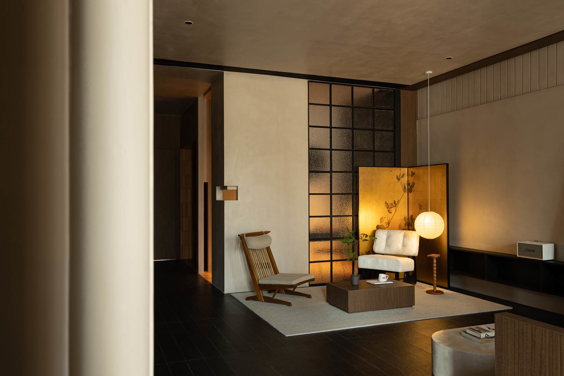 A minimalist living room with neutral-toned textiles, featuring a white armchair, a low wooden table, and a spherical lamp.
