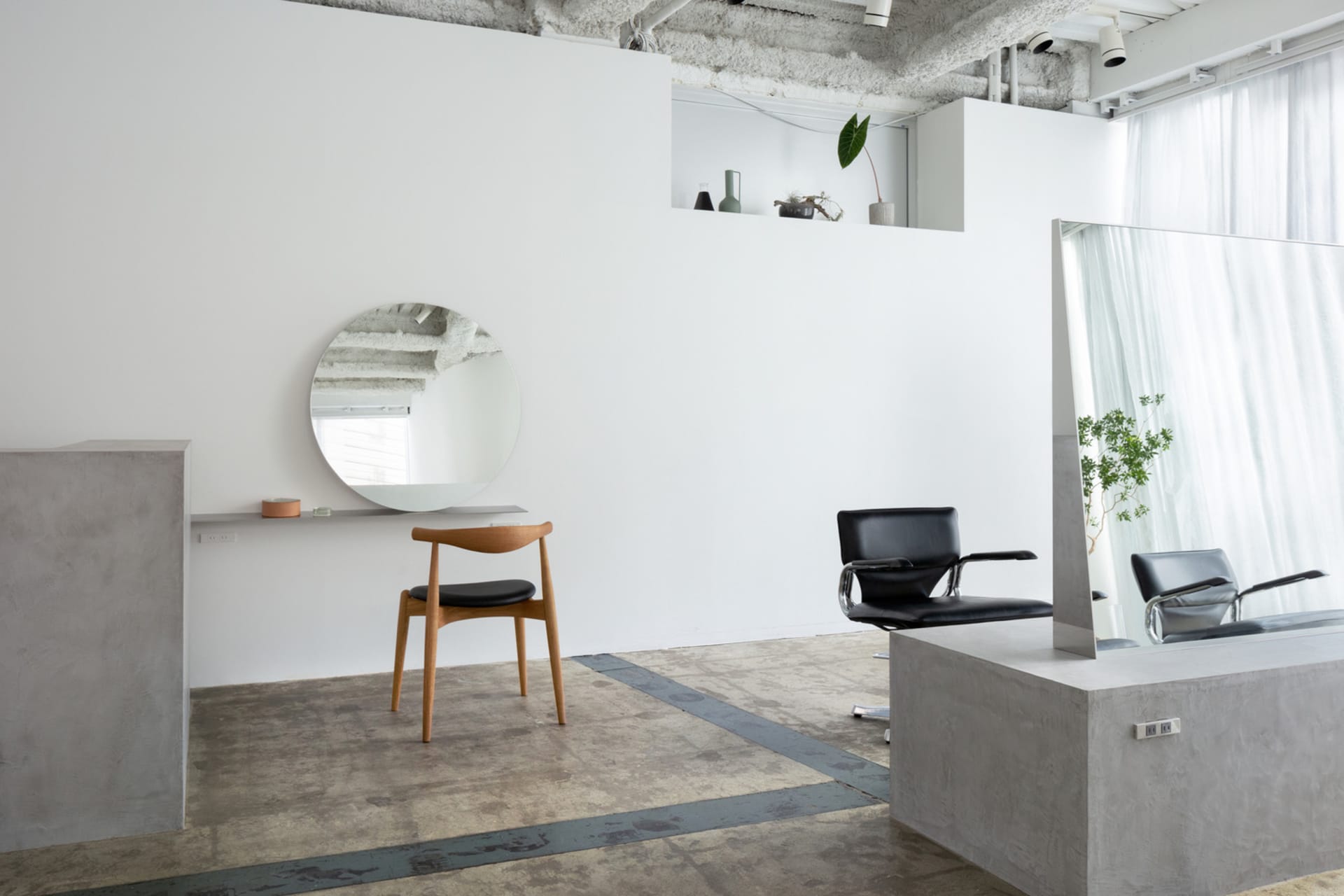 A modern hair salon featuring a minimalist design with concrete flooring and walls.