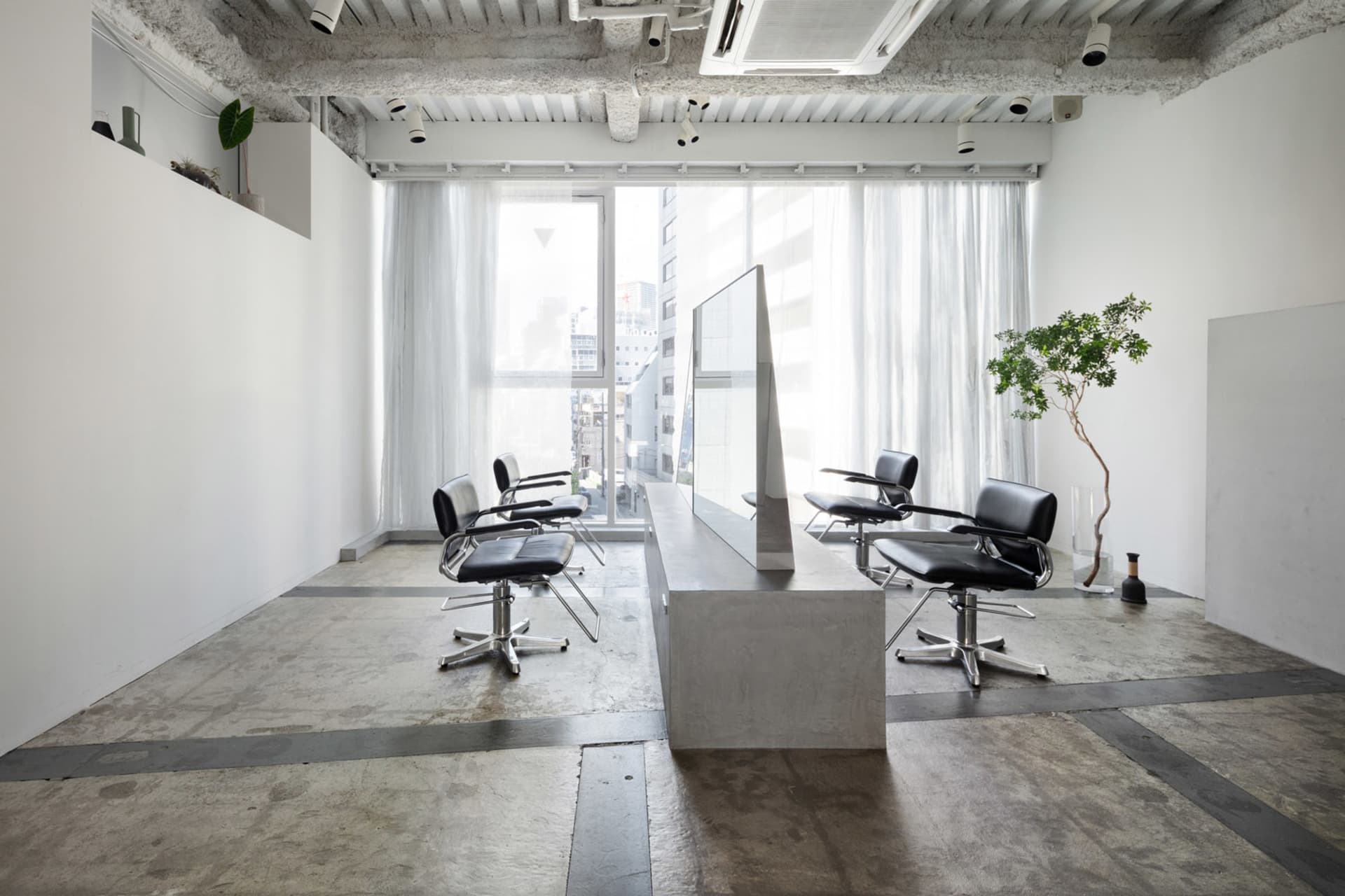 A minimalist modern hair salon with white walls, black chairs, and a concrete floor.