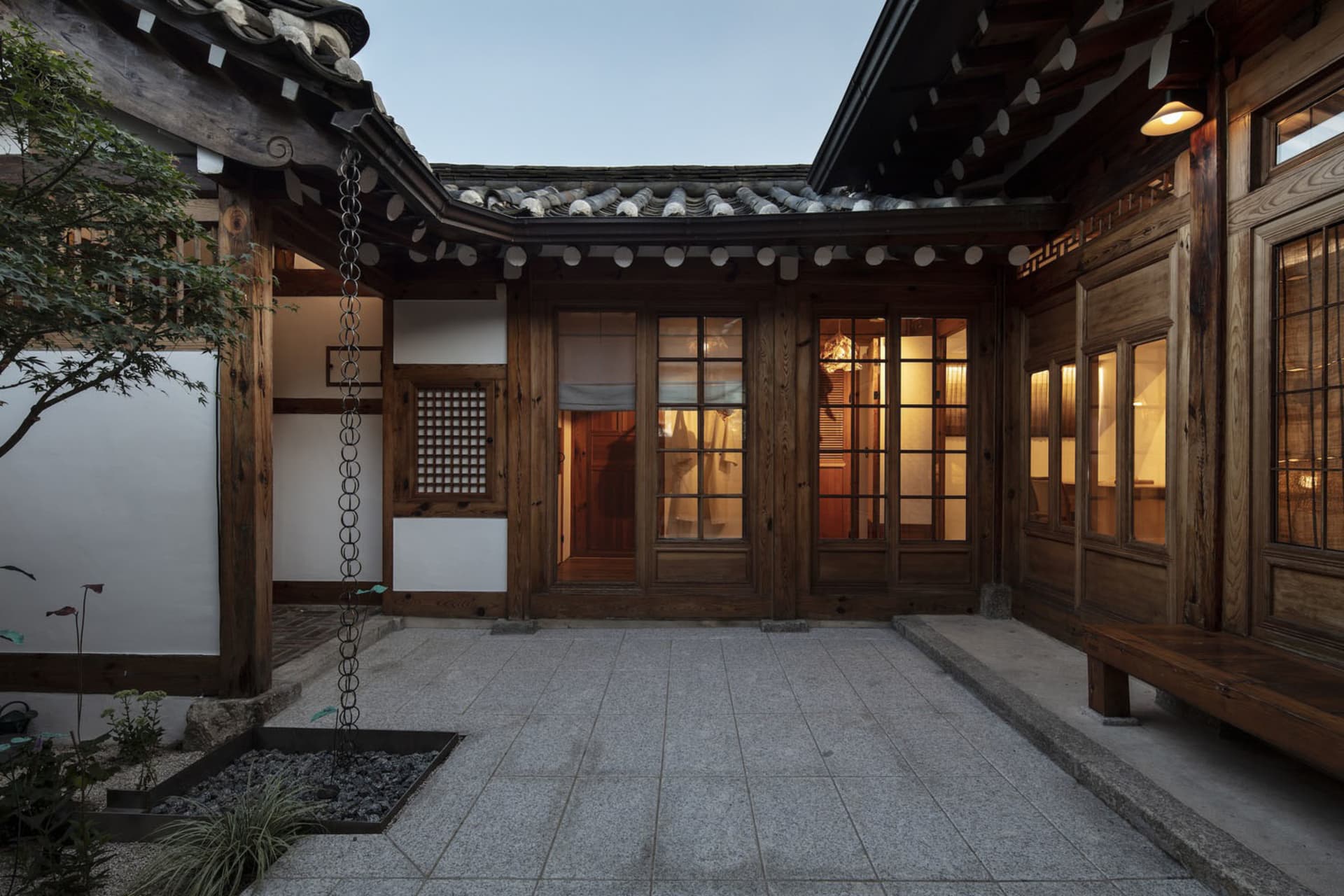A traditional wooden residence interior with a courtyard and lit rooms.