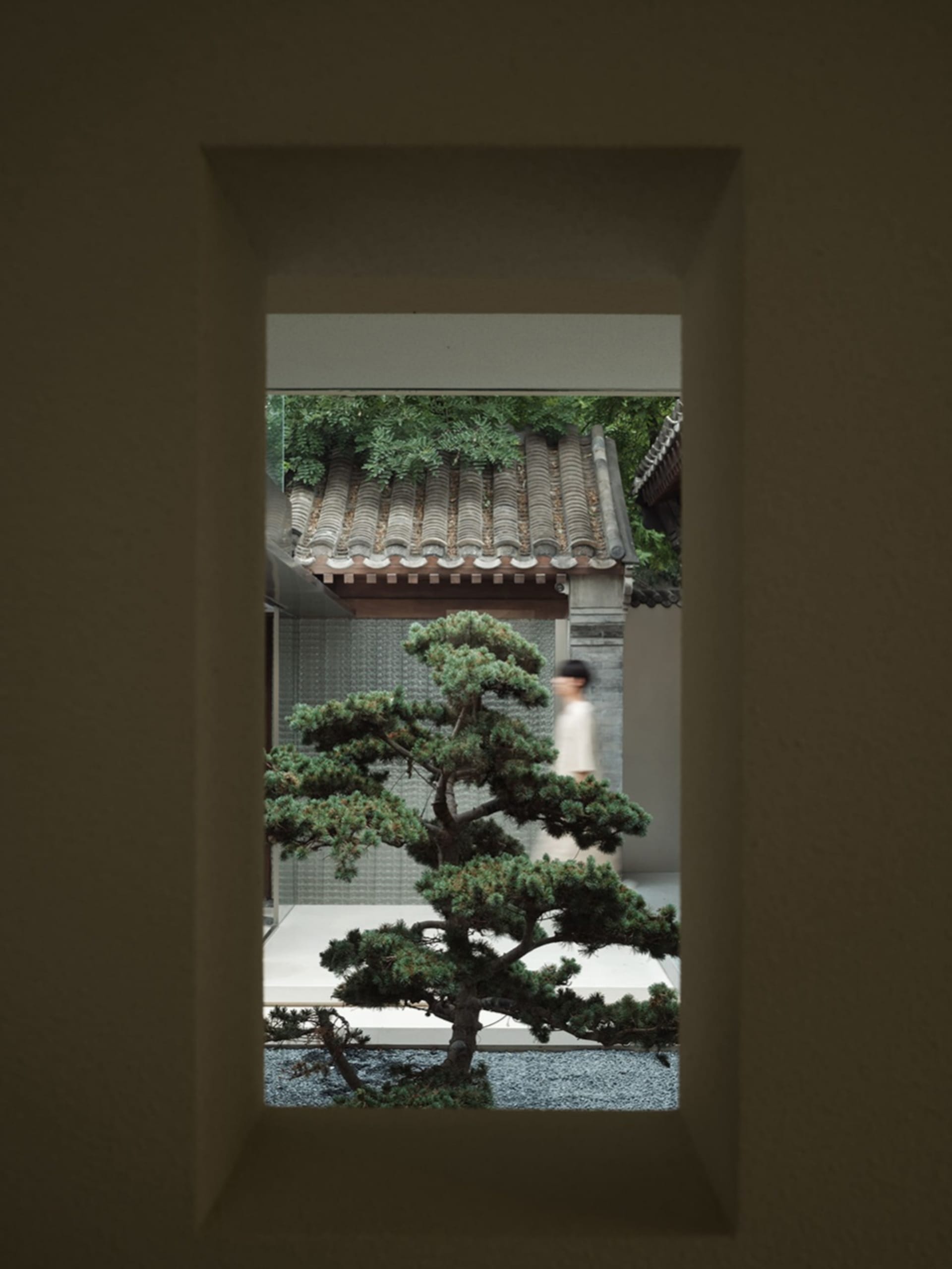 A serene outdoor view framed by a window, featuring stone garden elements, gravel pathways, and lush greenery.