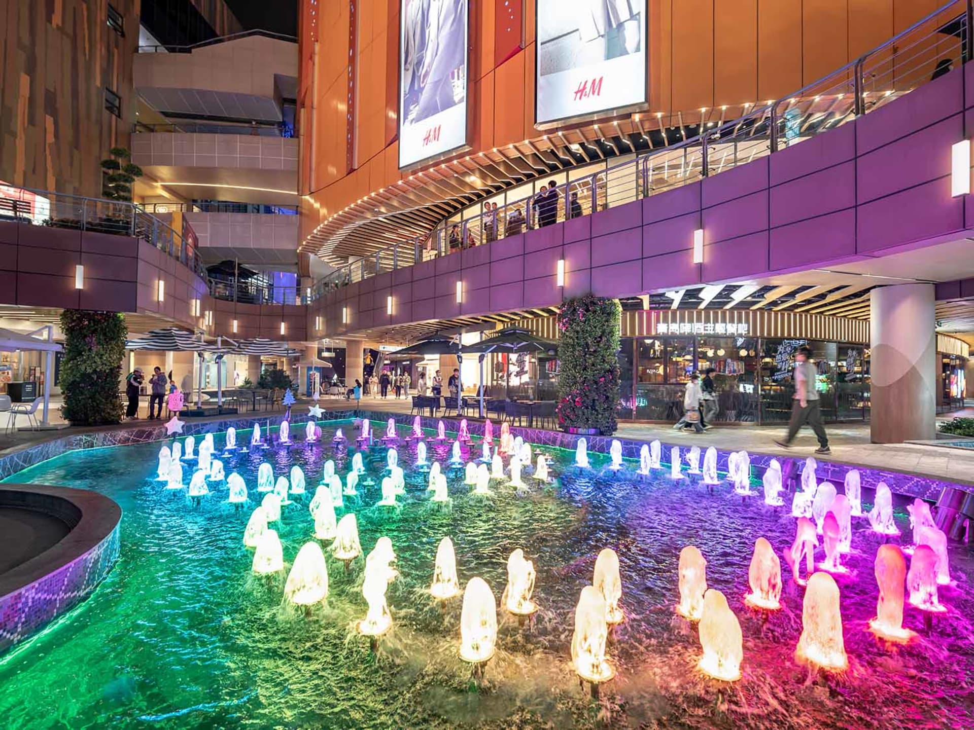A brightly illuminated water fountain at night with colorful lights and surrounding greenery.