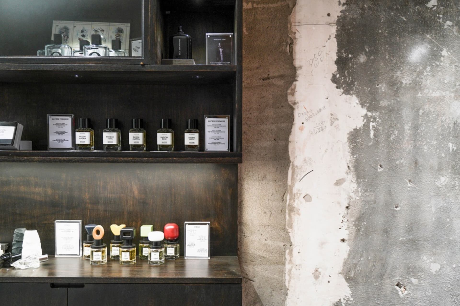 A set of perfume bottles displayed on a wooden shelf next to a concrete wall.