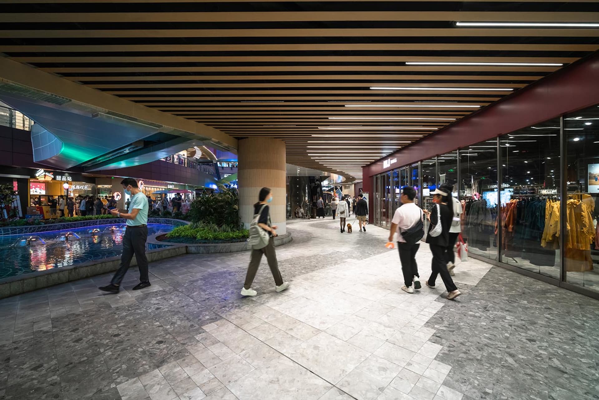 People walking in a modern shopping mall featuring concrete, glass, and tile flooring.