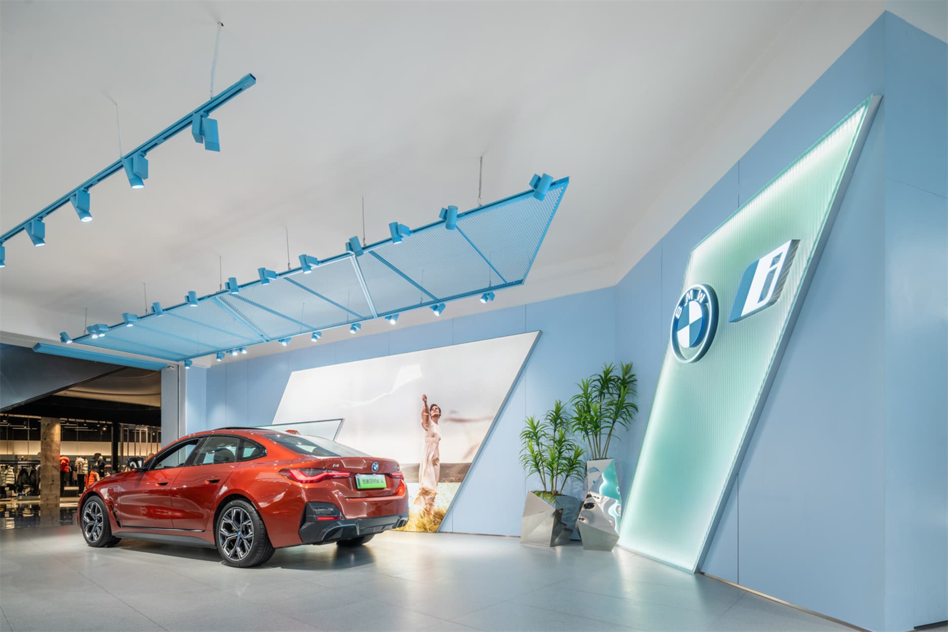 A modern car dealership showroom with a red car on display, blue lighting, and green plants.