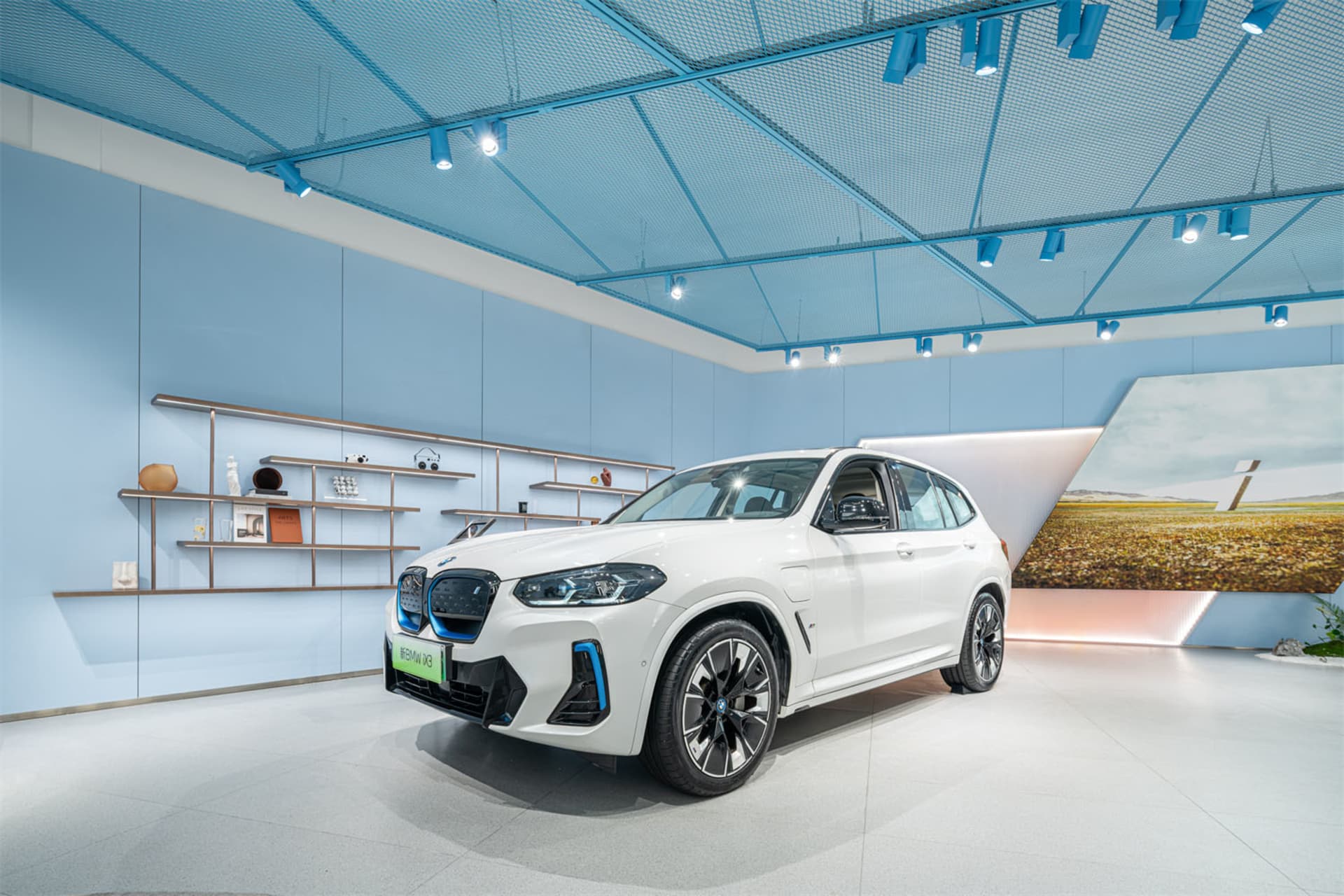 A white BMW SUV with blue accents displayed in a modern showroom with blue ceiling panels.