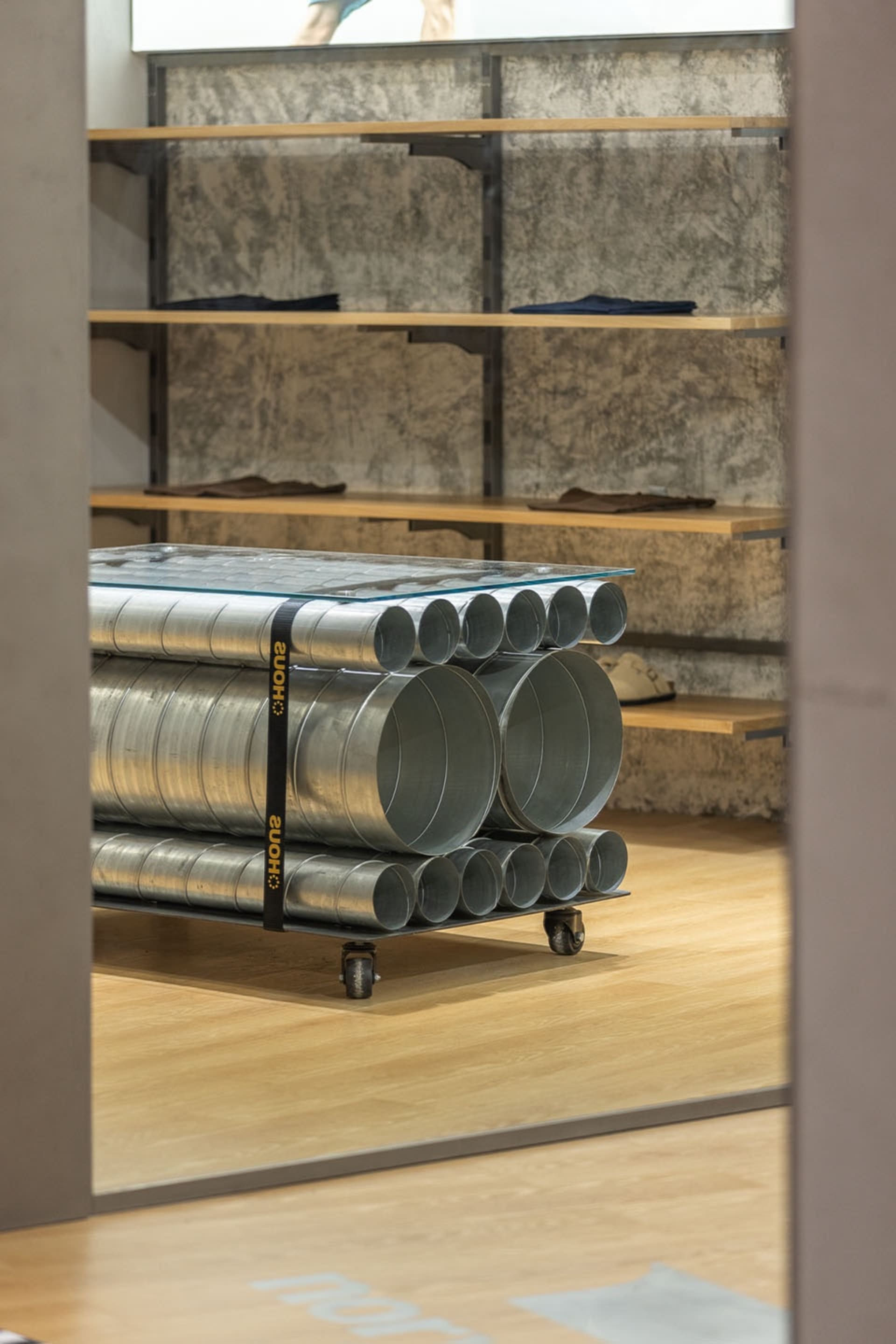 Metal pipes stacked in a store interior with glass top, wooden floor, and concrete walls.