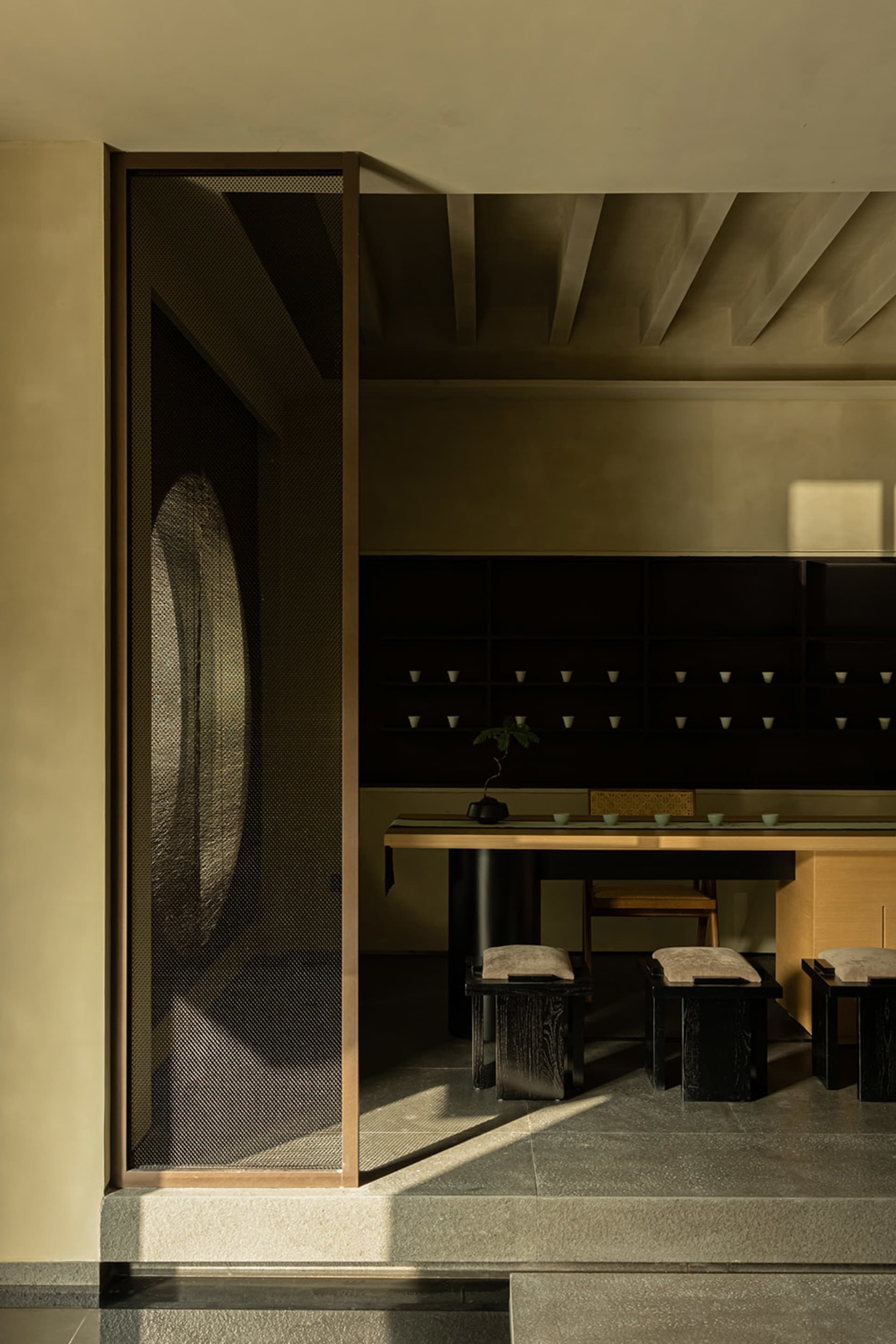 A minimalist tea room featuring wooden furniture, stone flooring, and glass elements.