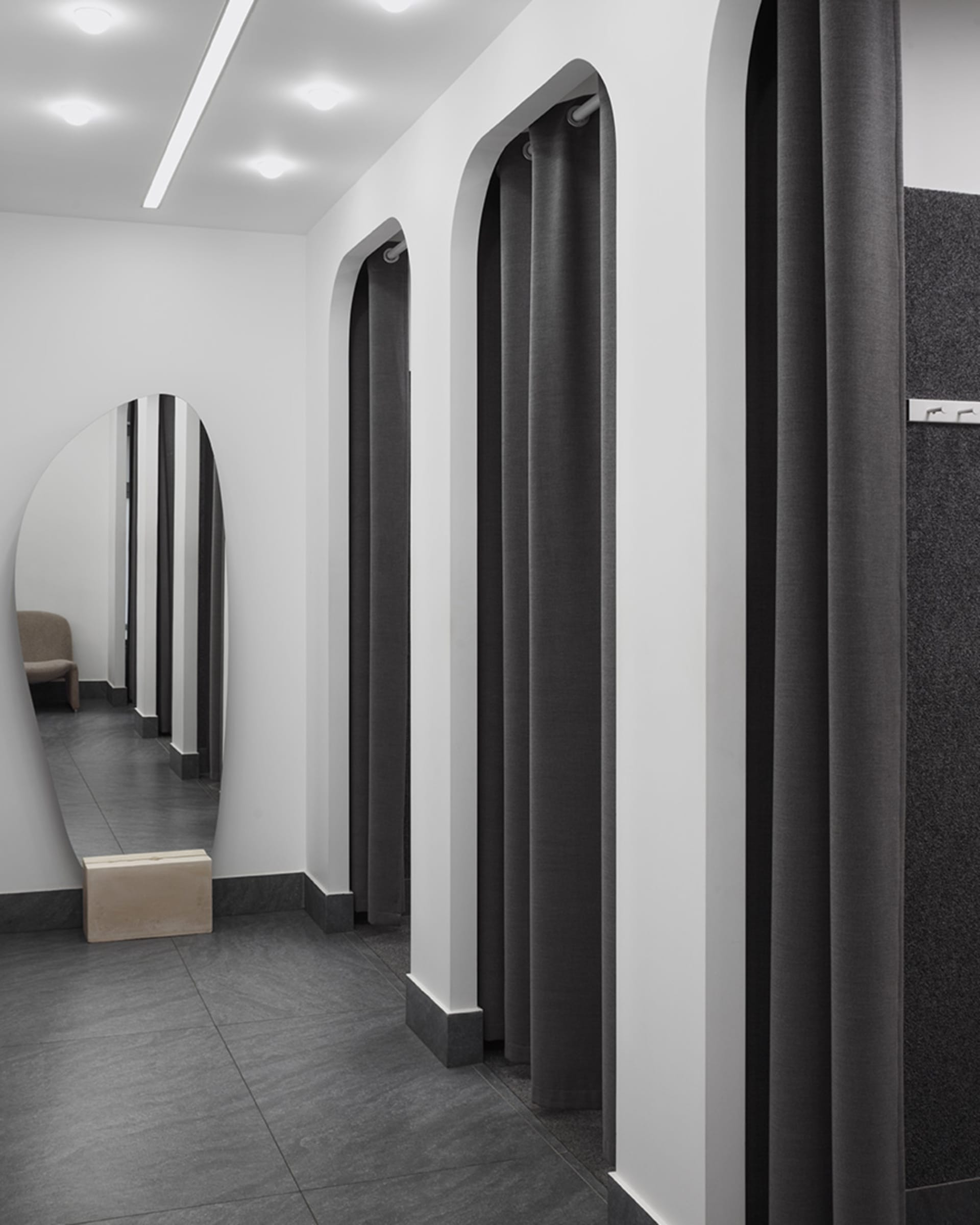 Industrial-style clothing store dressing rooms with gray textiles, white walls, and black tiles.