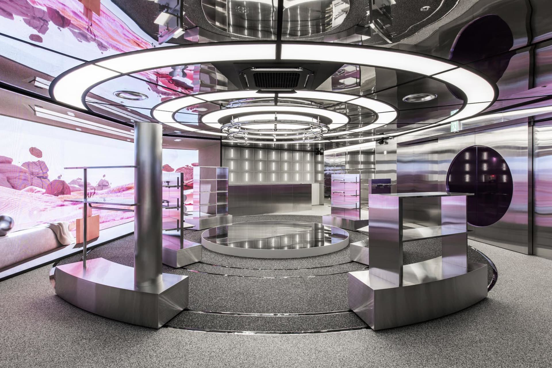 A futuristic, metallic interior design featuring a circular stage with a pink and purple color scheme.