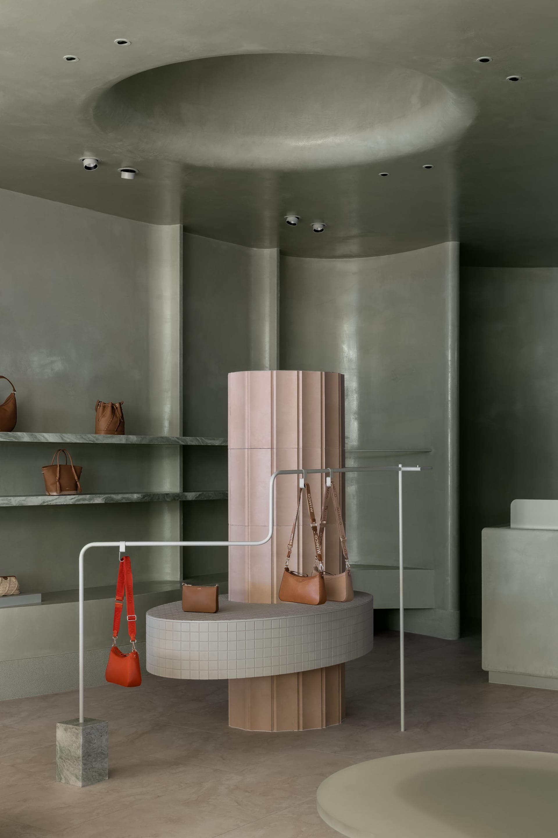 A minimalist retail space features concrete walls and flooring, with bags displayed on a cylindrical pedestal.