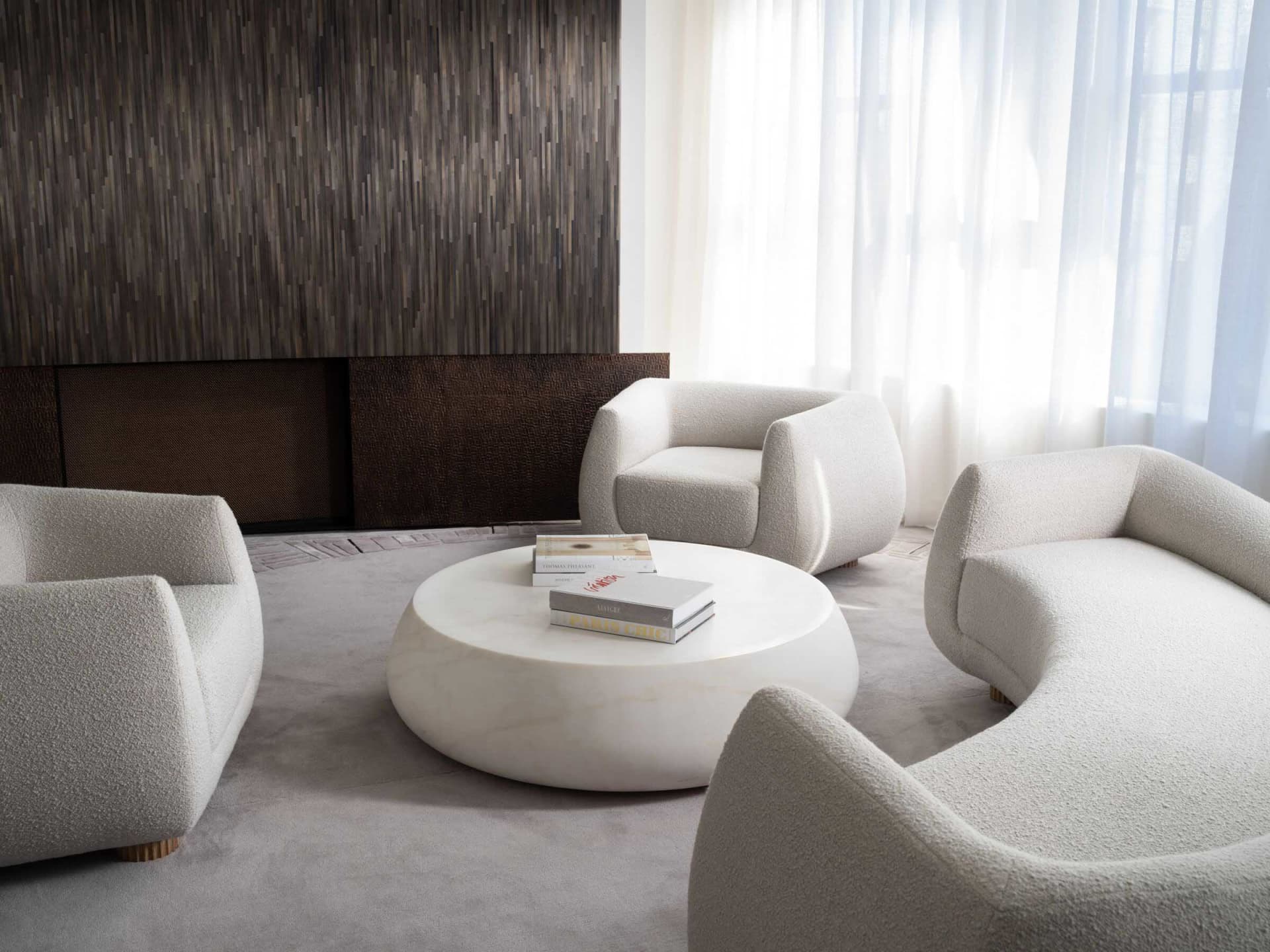 A modern living room with round white fabric furniture and a marble center table under a large window with sheer curtains.
