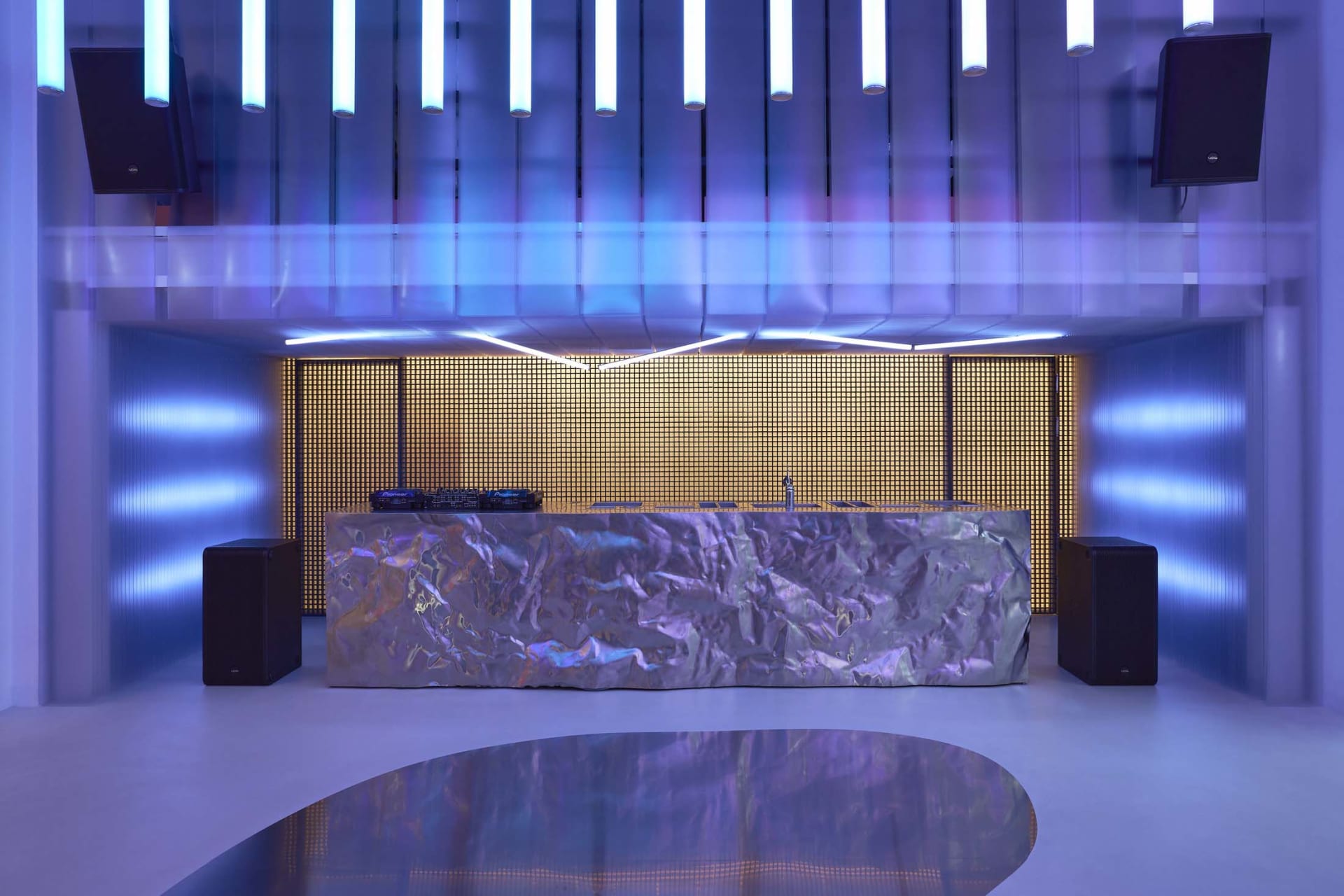 Modern, minimalist DJ booth with metallic surface and futuristic lighting in a club setting.