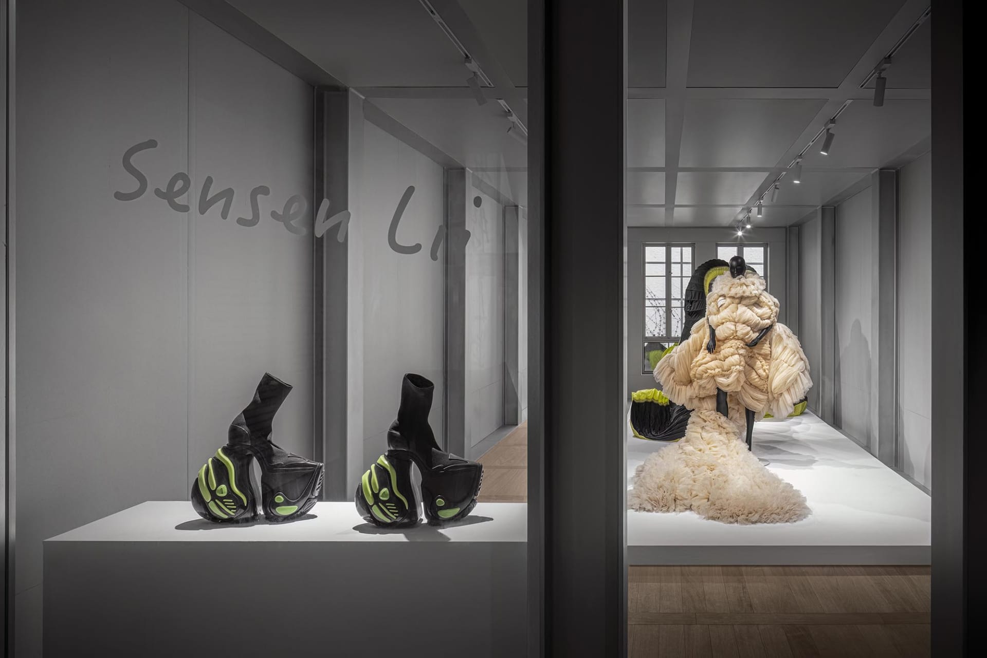 A display featuring futuristic black and green high-heeled shoes and a intricately draped, beige textile piece in an industri