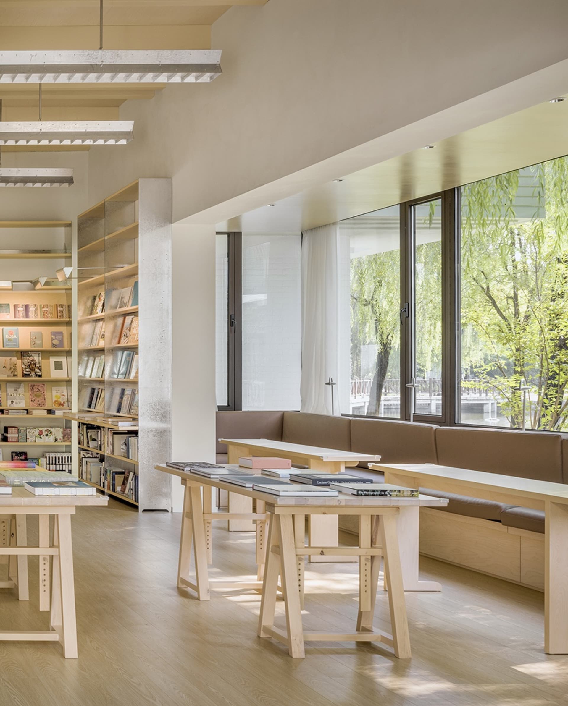 簡約風格的圖書館室內,搭配木質桌椅、書架,以及靠近大窗的閱讀區。