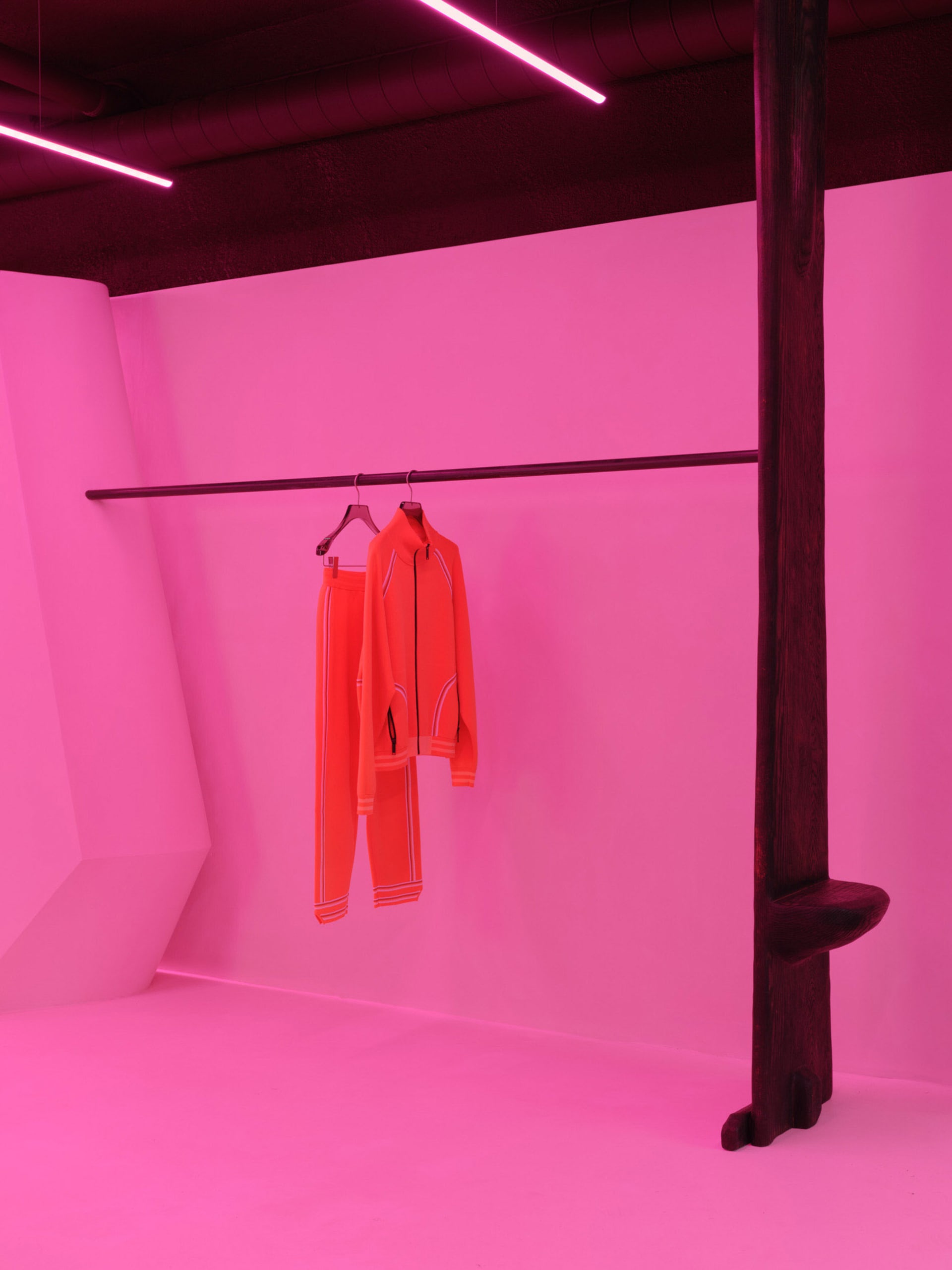 現代服裝展示，亮紅色外套與長褲懸掛在黑色衣桿上。