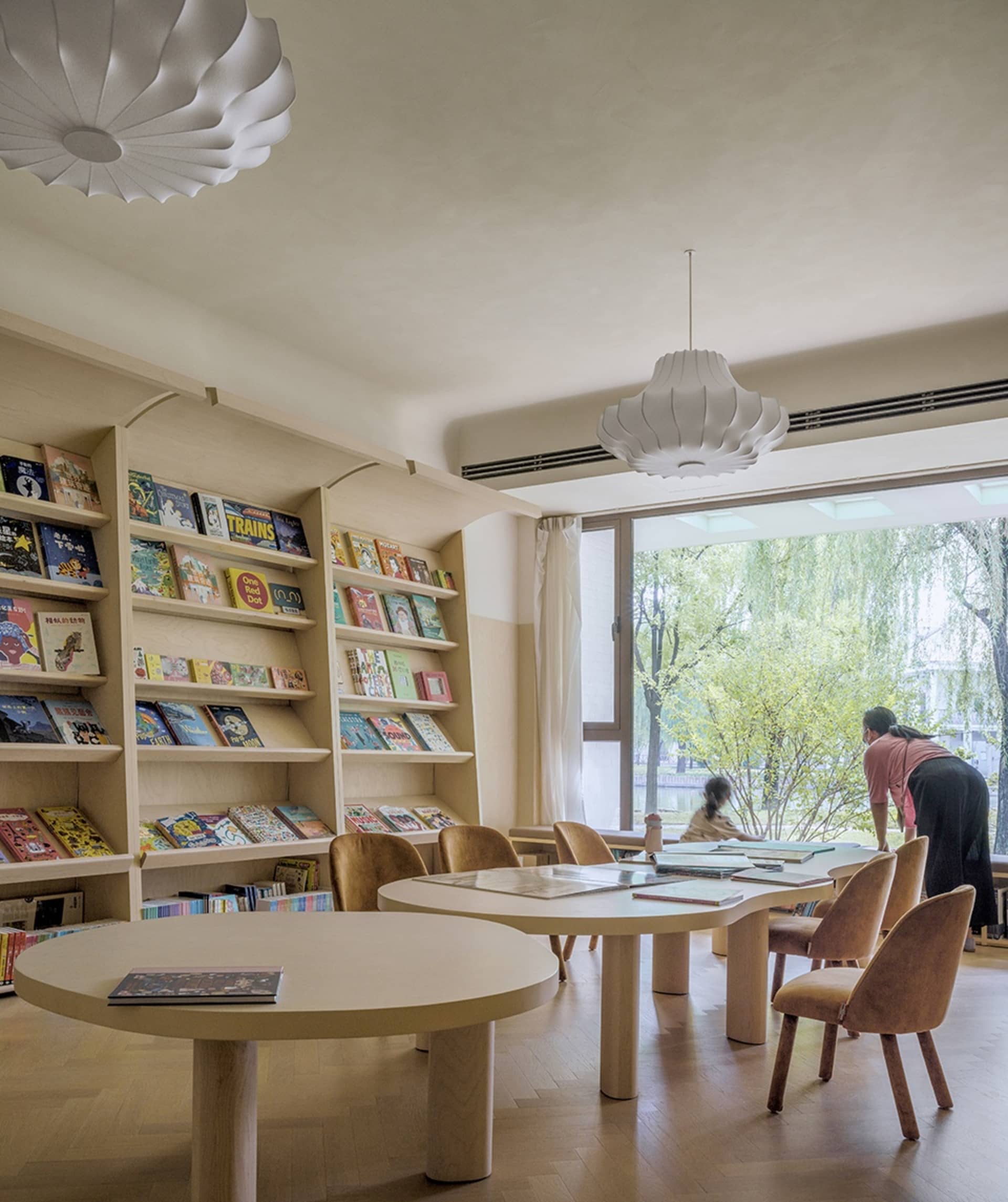 A modern library with wooden shelves and glass walls, featuring comfortable seating and a large window.