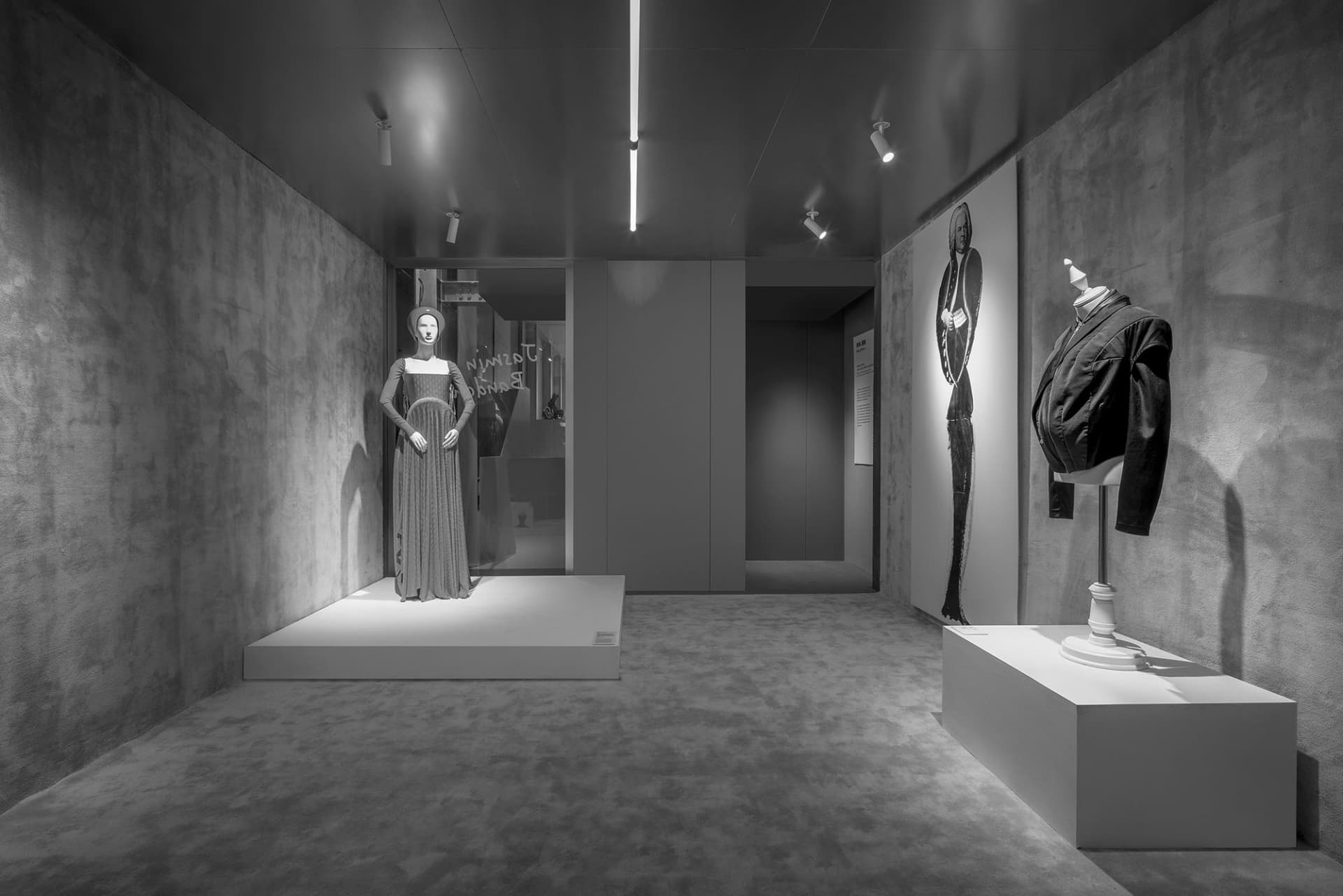 A modern fashion exhibit featuring concrete interior design, with mannequins dressed in elegant clothing and artwork on the w
