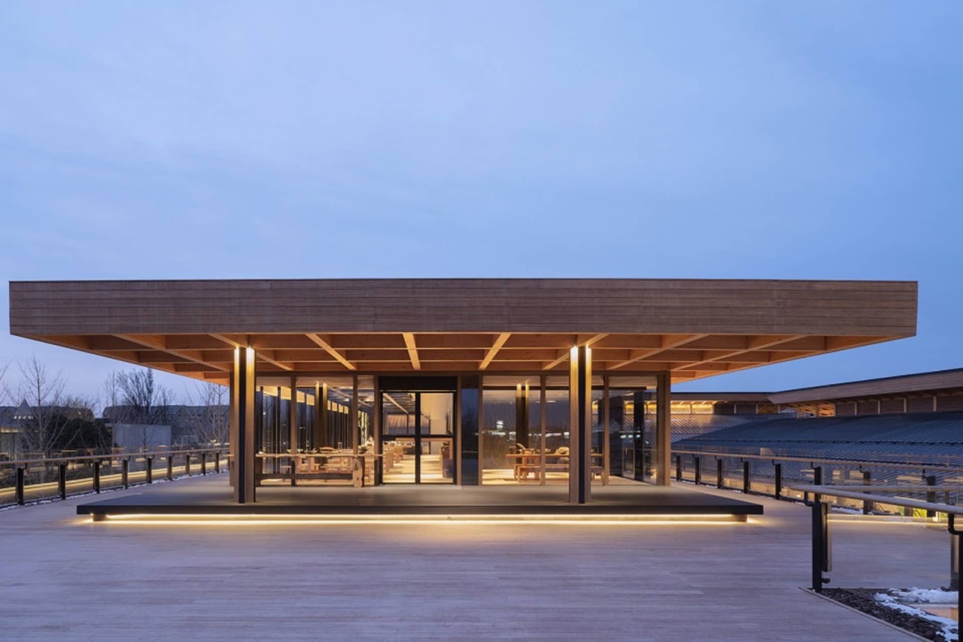 Modern restaurant exterior with wooden beams and glass walls against a clear sky.