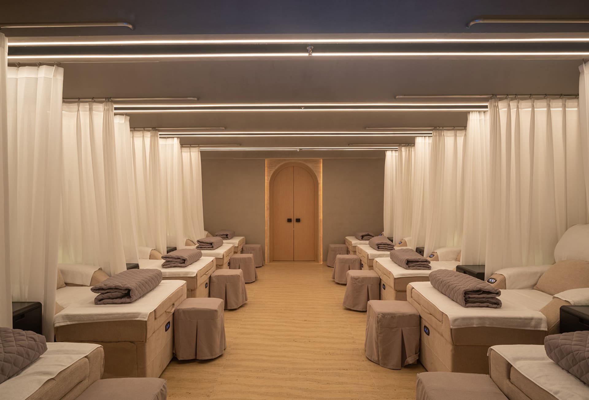Rows of spa beds with fabric tops and wooden flooring, separated by curtains in a spa interior.