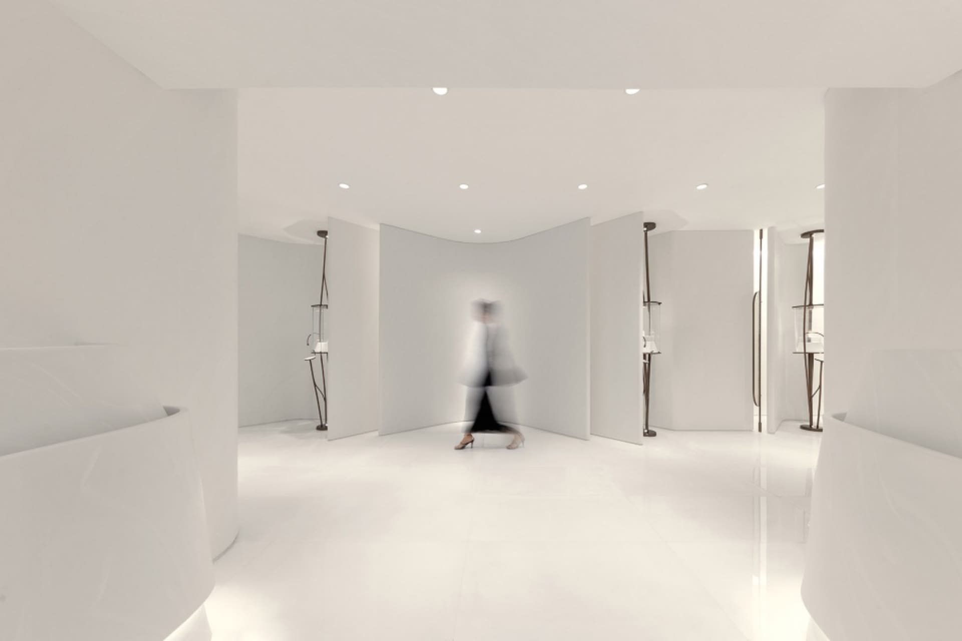 A minimalist white interior space with curved walls and a person walking through the corridor.