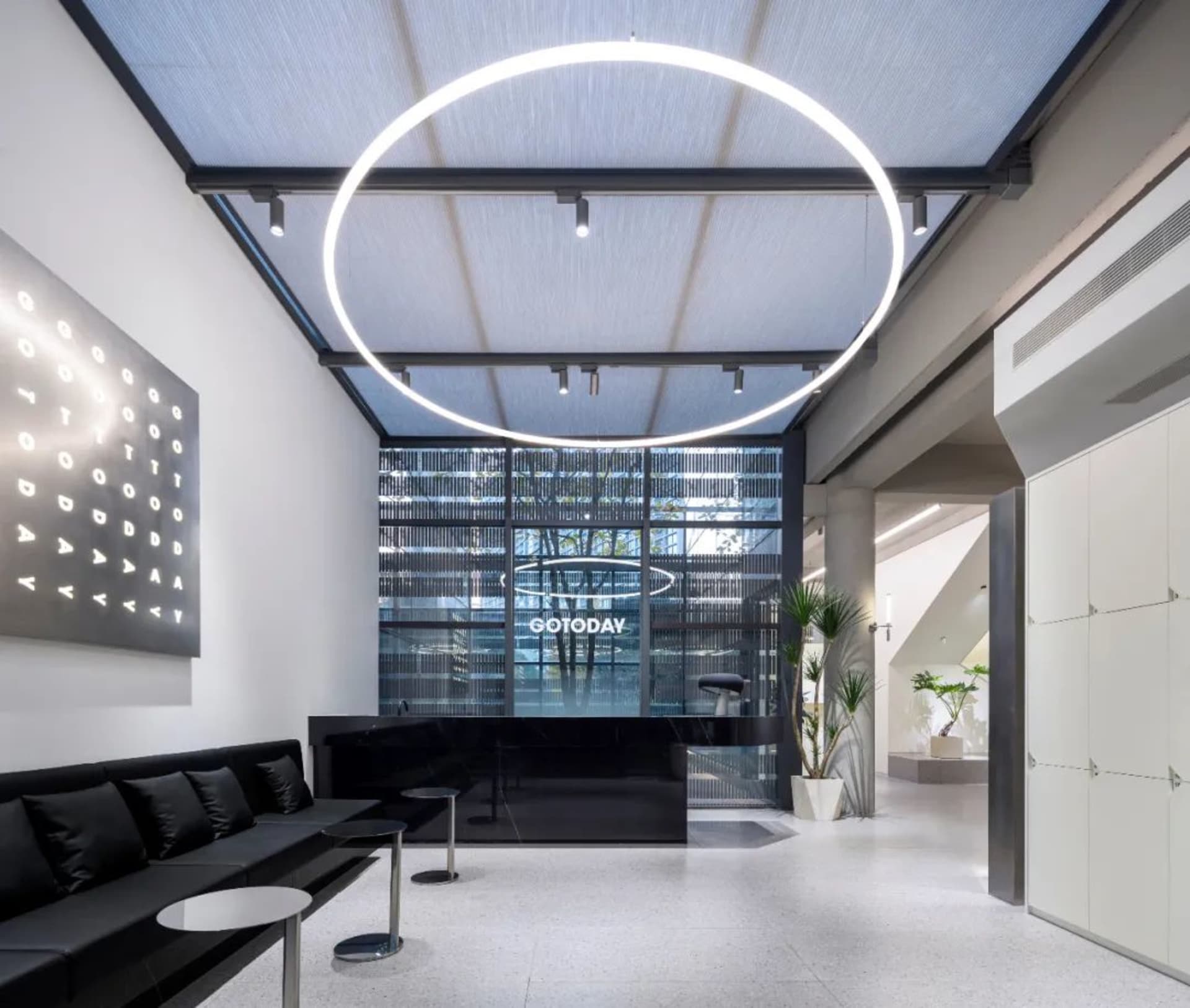 A modern industrial office lobby with a circular light fixture, black furniture, and concrete flooring.