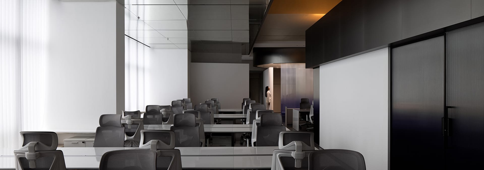 Modern office space with long desks and chairs arranged in rows.