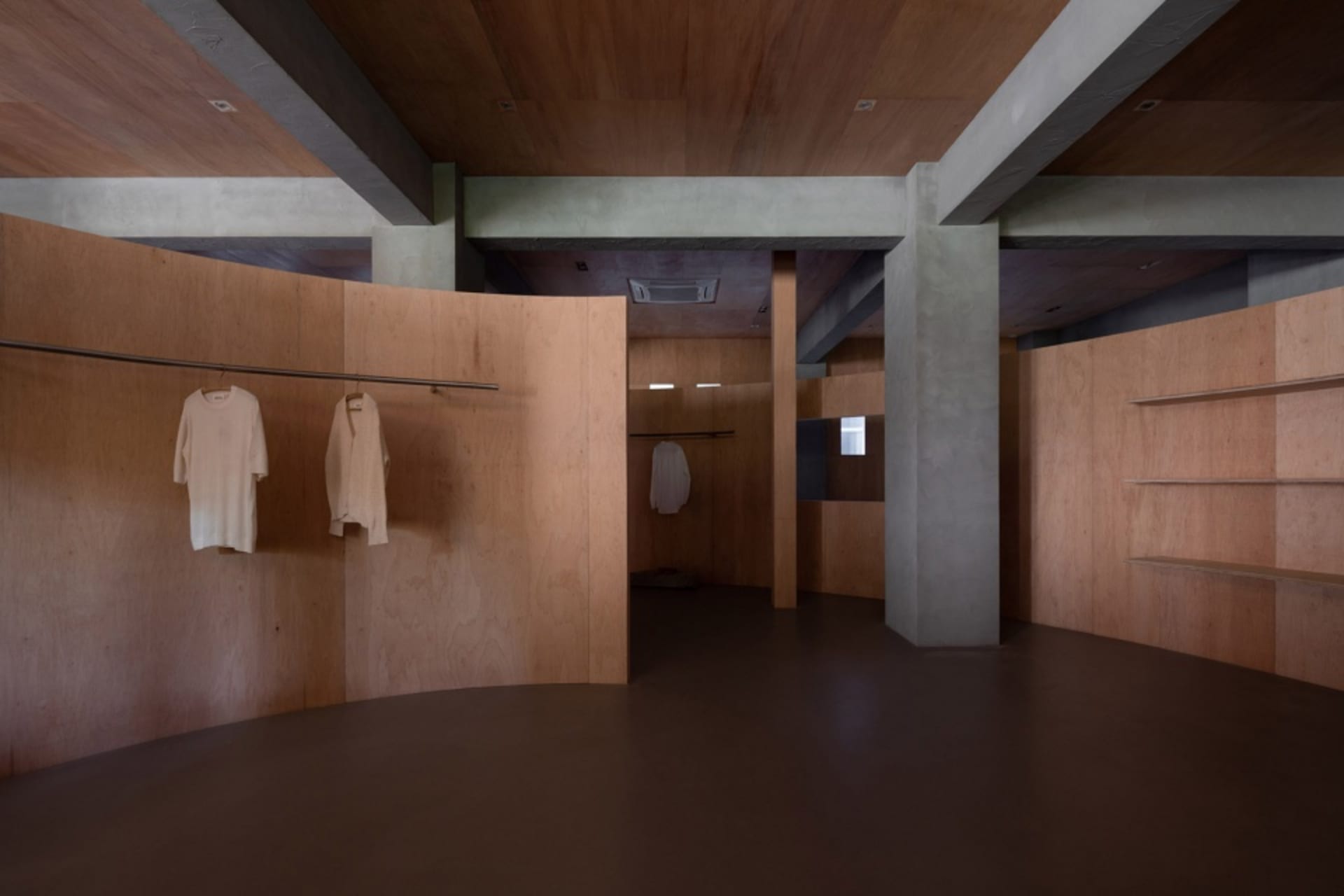 A modern clothing store with wood-paneled walls and floors, featuring minimalistic design elements and white garments hanging