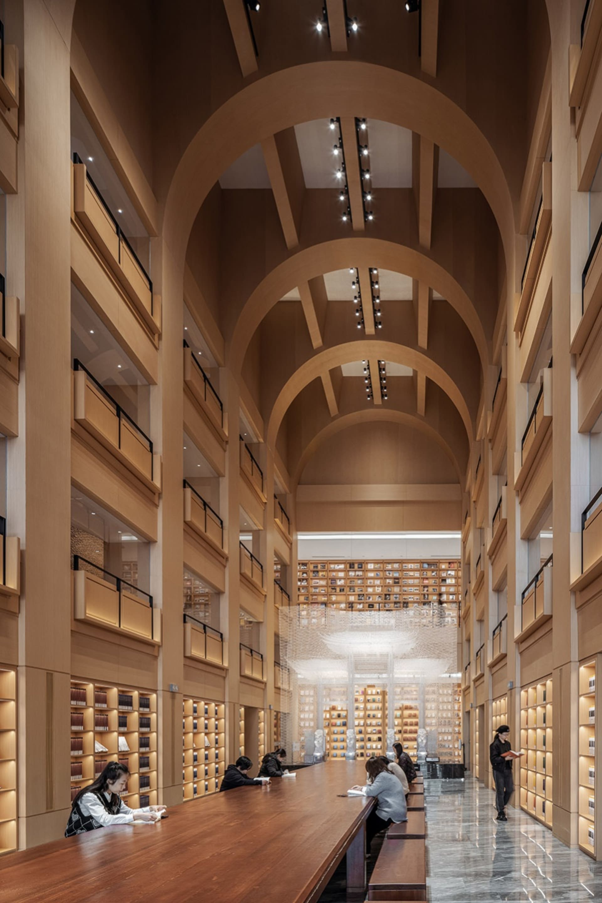 People sitting at tables in a spacious library with wooden shelves and high ceilings.