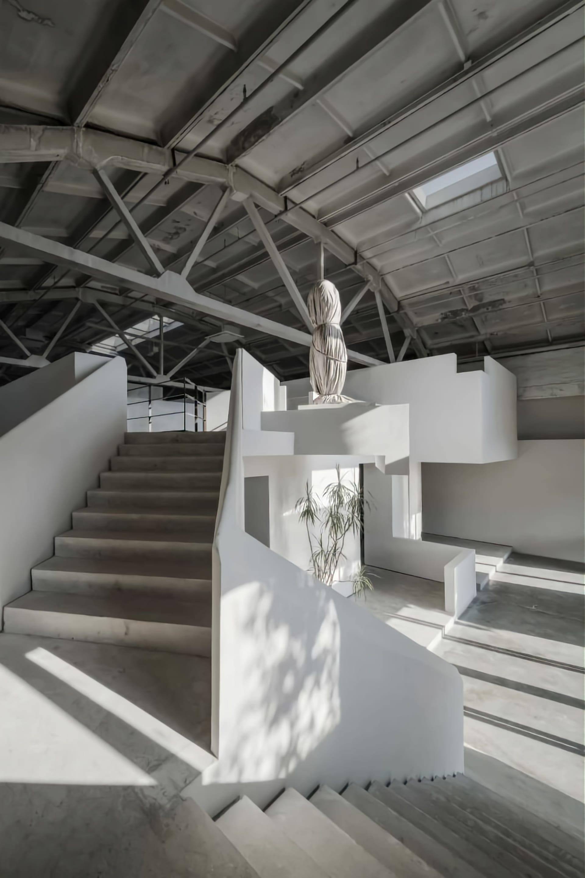 A minimalist interior space with exposed concrete walls, spiral staircase, and a white, modern sculpture.