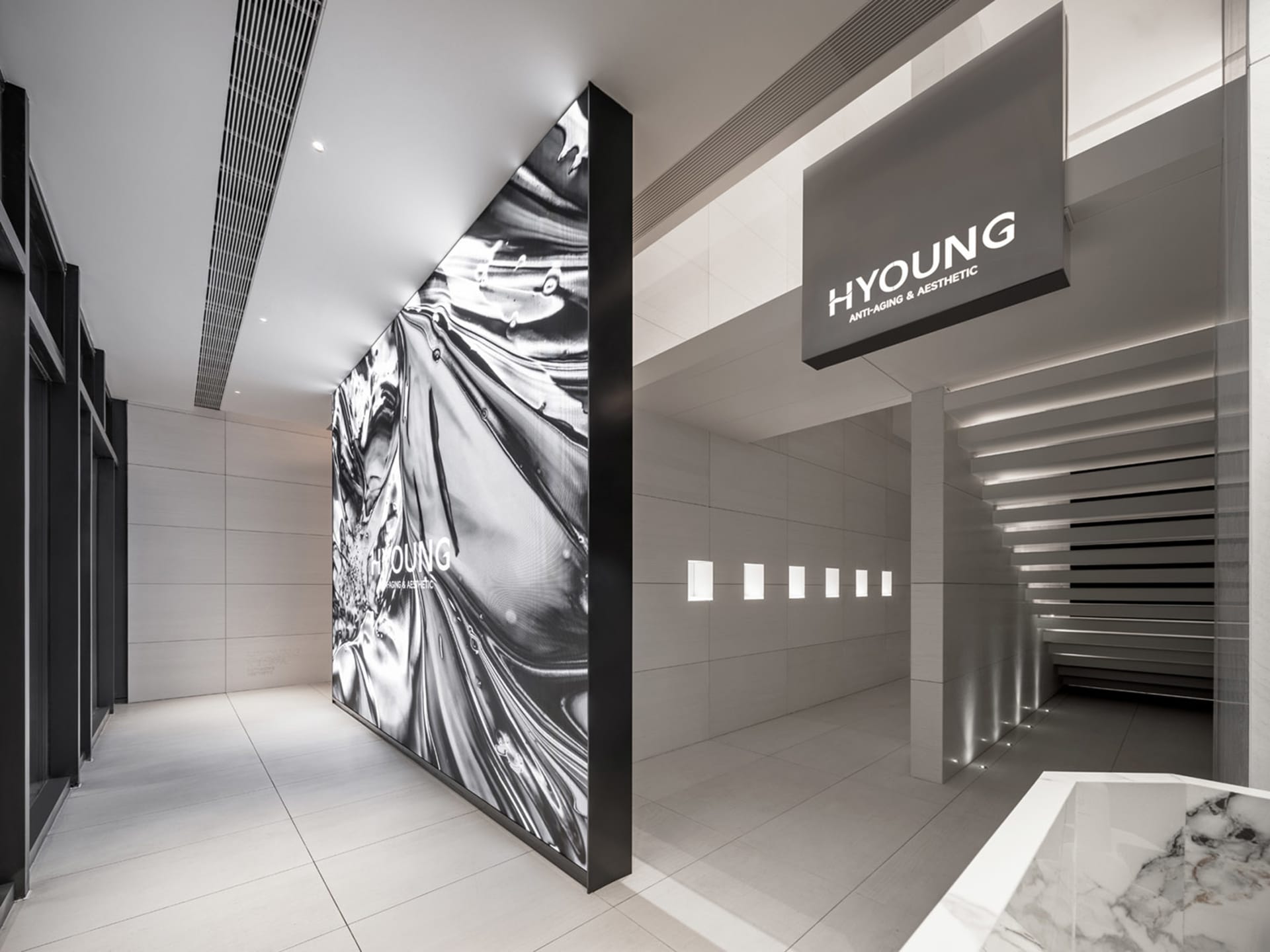 Modern, minimalist medical clinic with a metal-clad wall, illuminated by recessed lighting and featuring marble flooring.