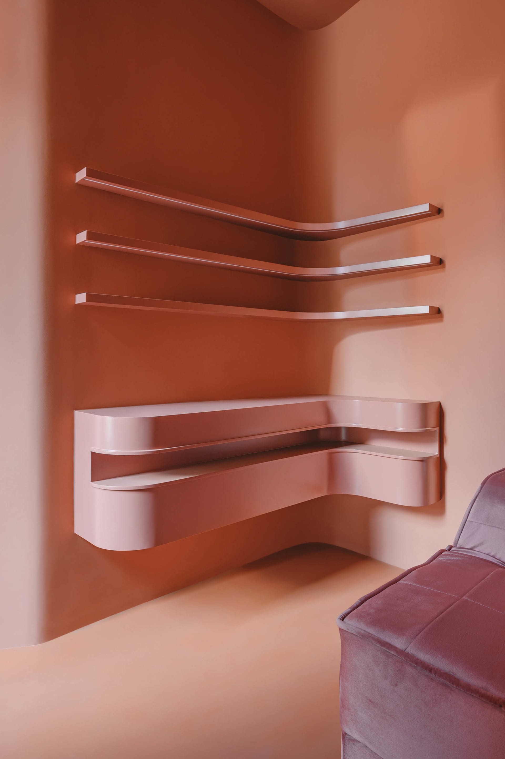 Modern minimalist metallic floating shelves mounted on a peach-colored wall.