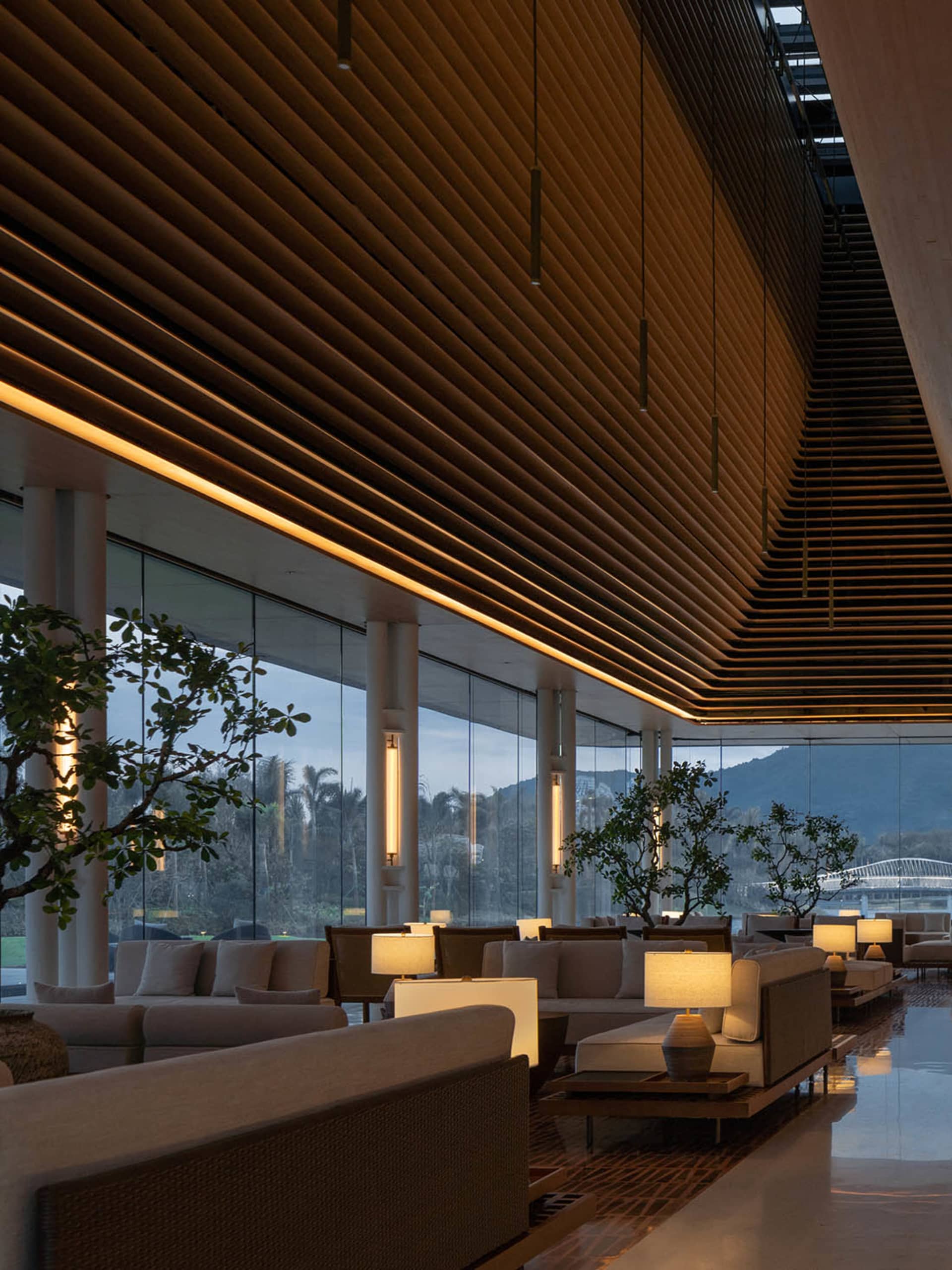 A modern hotel lobby with wooden paneling and glass walls, featuring comfortable seating arrangements and natural lighting.