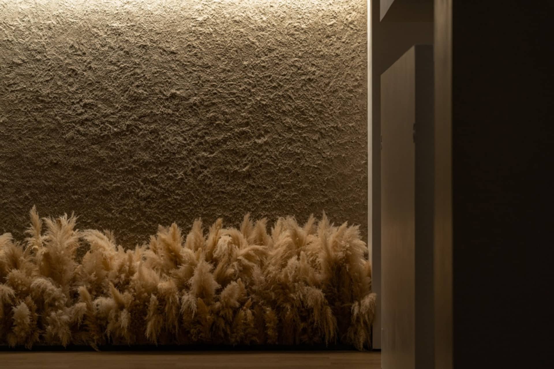 A textured, beige-colored wall adorned with golden-yellow decorative grasses enhancing the ambiance of the space.