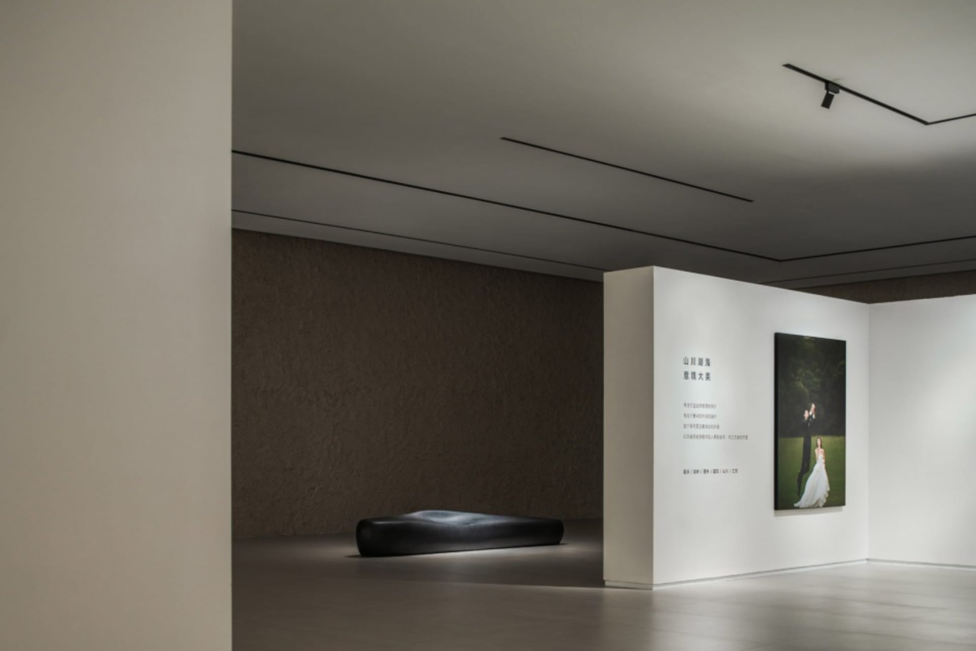 Modern minimalist photography gallery with a minimalist installation featuring a black bench and a framed photograph on the w