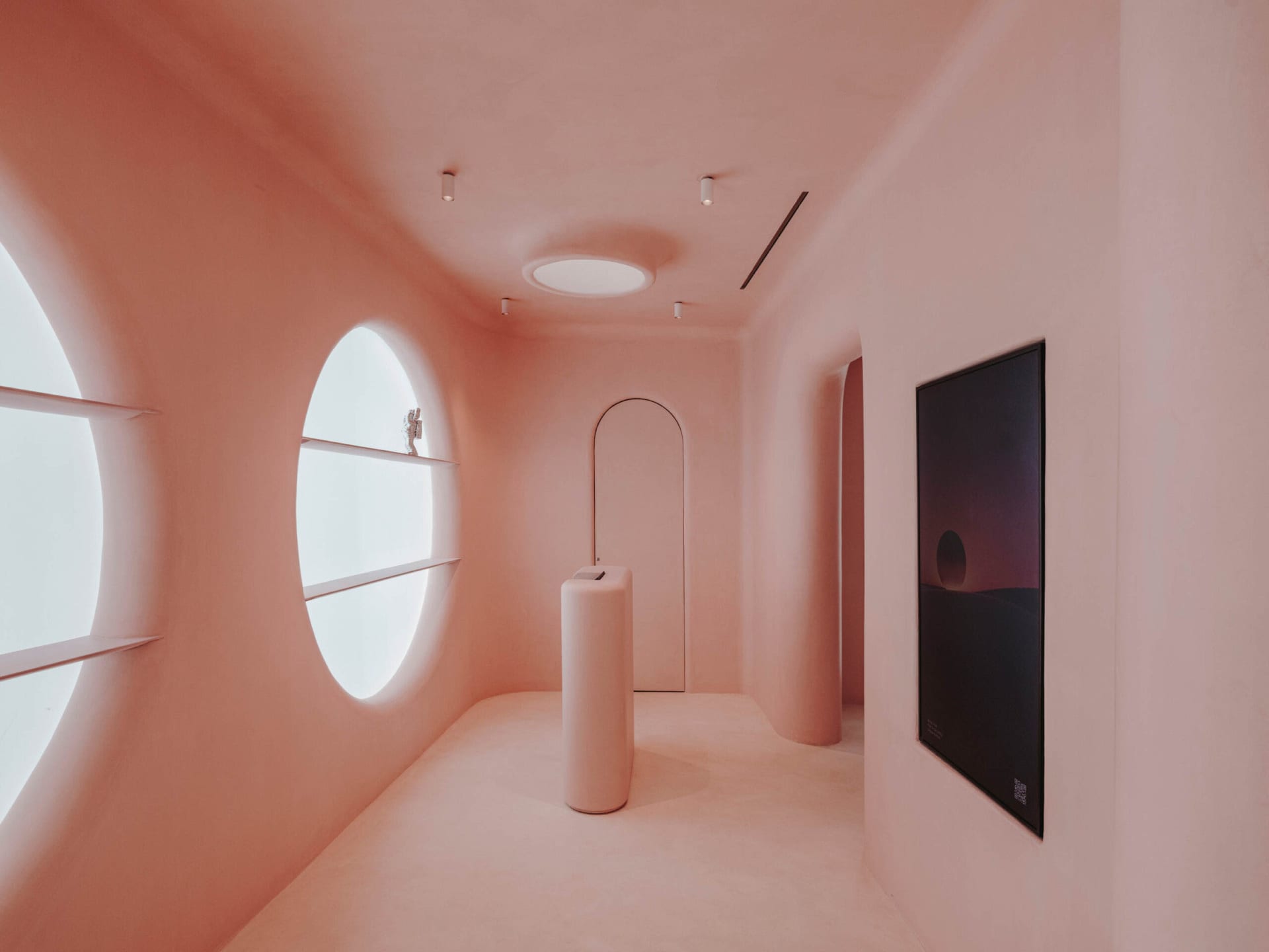 A minimalist interior design featuring walls painted pink with unique circular shapes and a single cylindrical pedestal.
