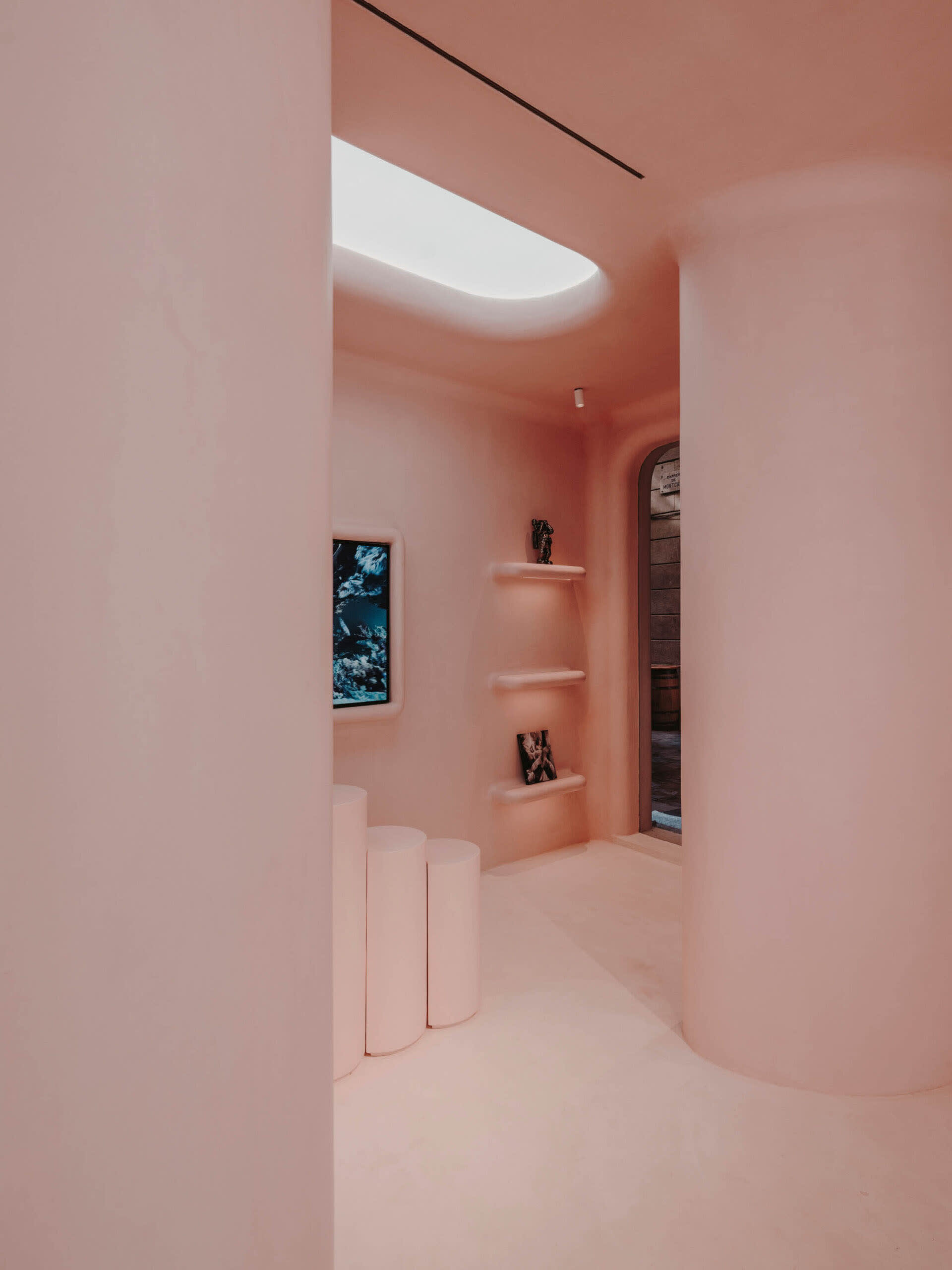 A minimalist interior with pink plaster walls, white cylindrical columns, and a skylight.