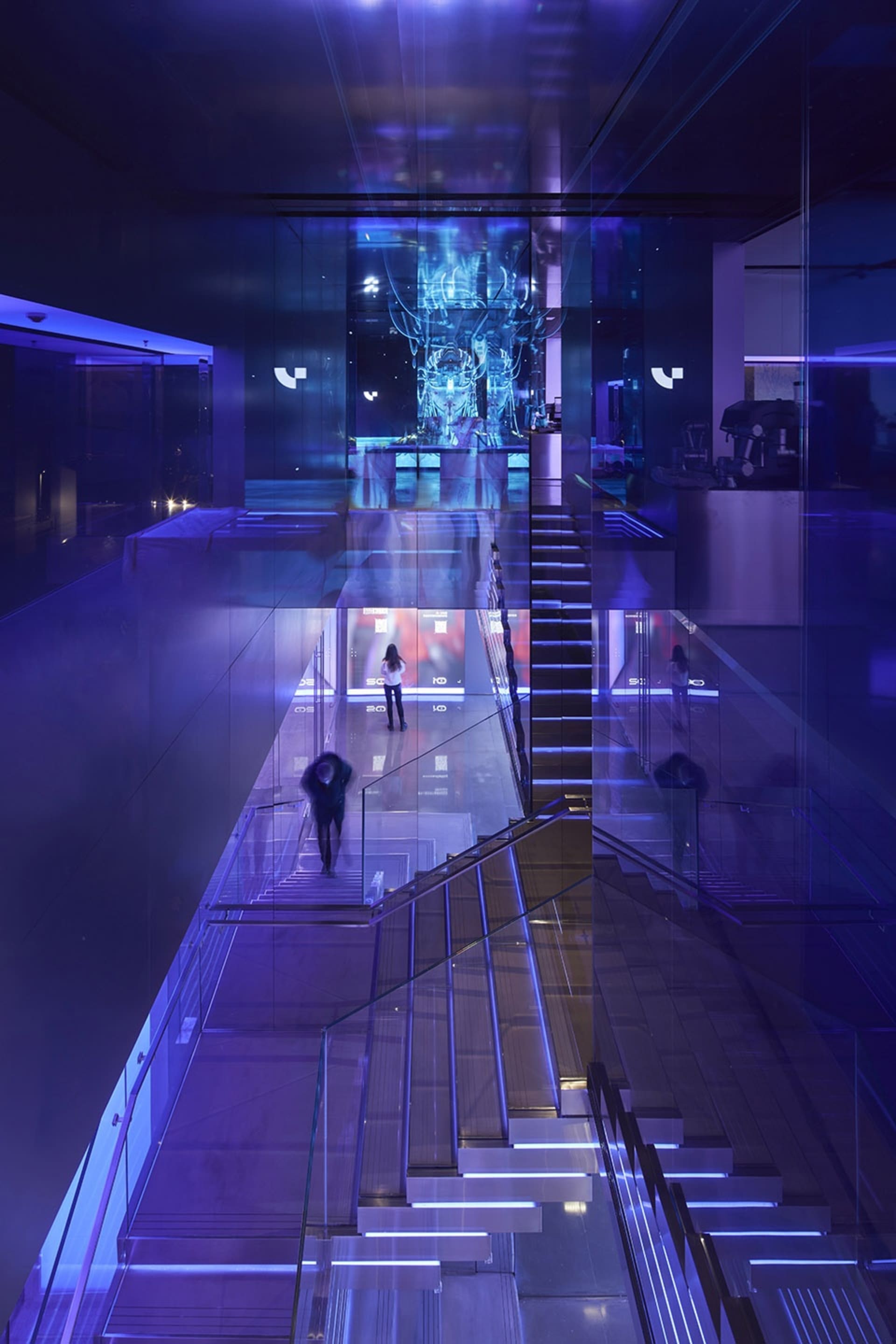 人們走過現代玻璃博物館展覽廳，藍色燈光照亮空間